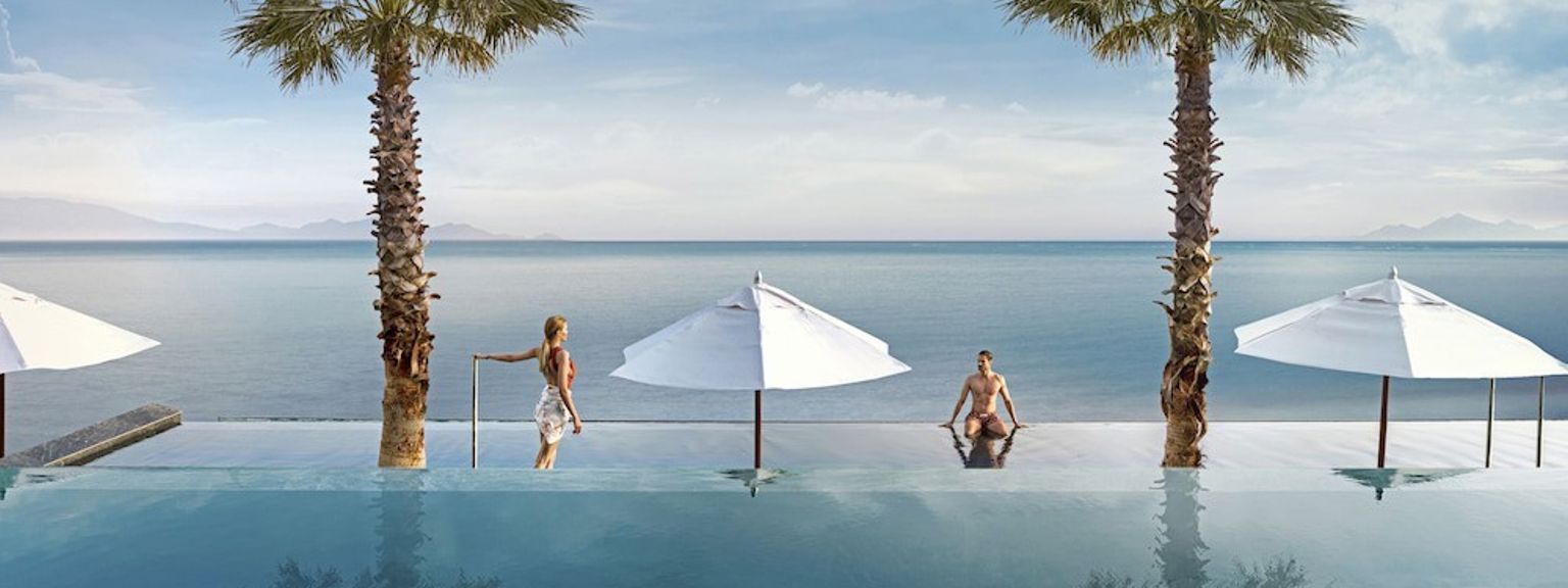 two people are sitting in a swimming pool next to palm trees overlooking the ocean.