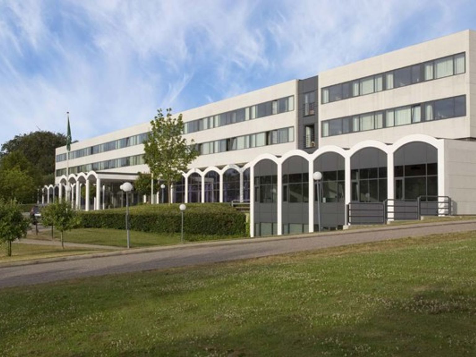 en stor bygning med mange vinduer sidder på toppen af en græsklædt bakke