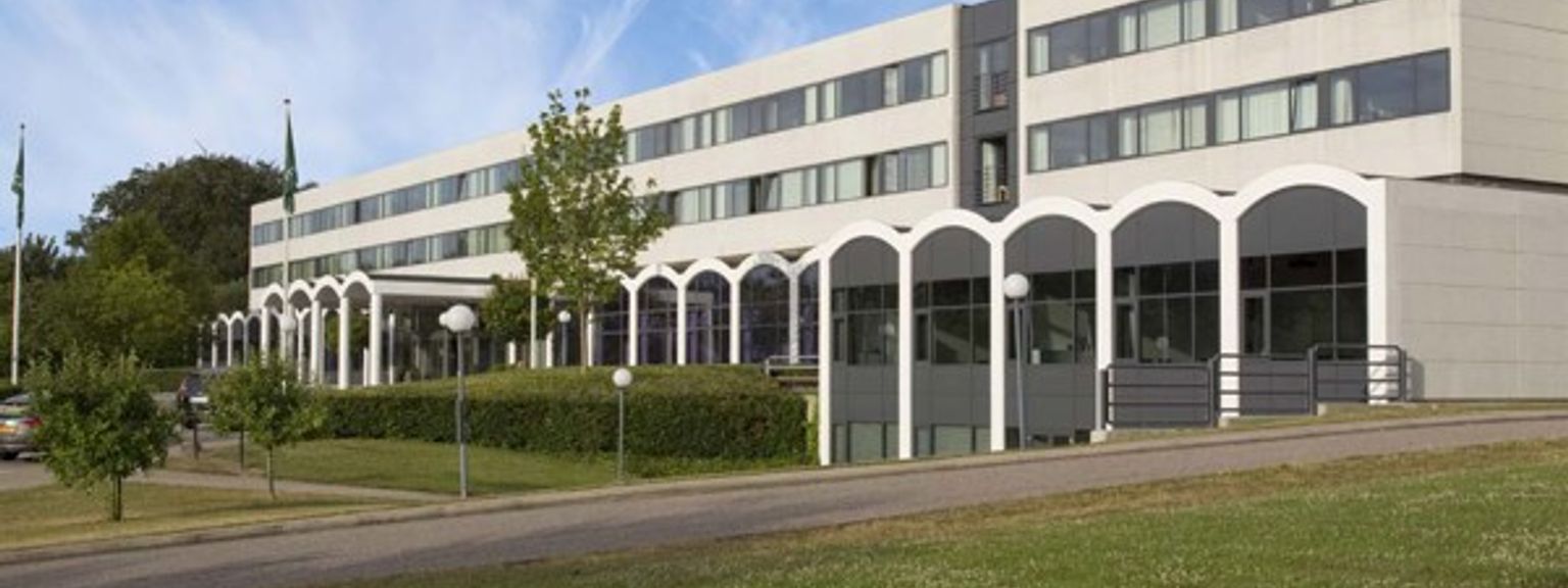 en stor bygning med mange vinduer sidder på toppen af en græsklædt bakke