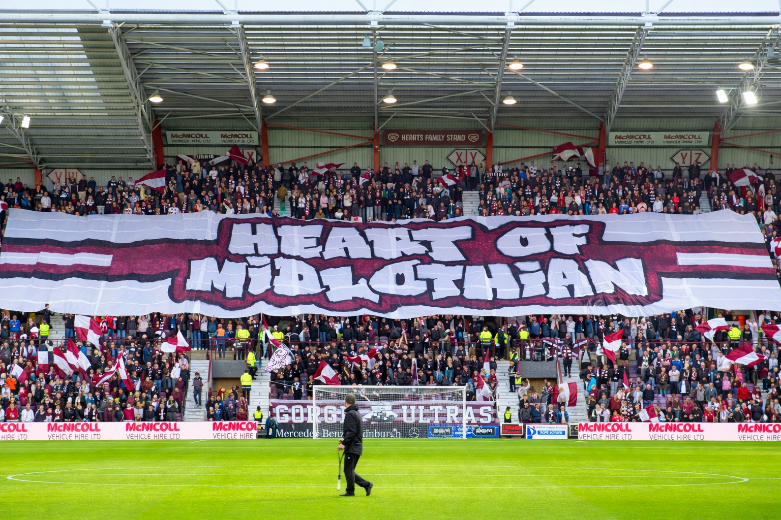 Een grote menigte voetbalfans in een stadion houdt een enorm spandoek omhoog met de tekst "HEART OF MIDLOTHIAN."