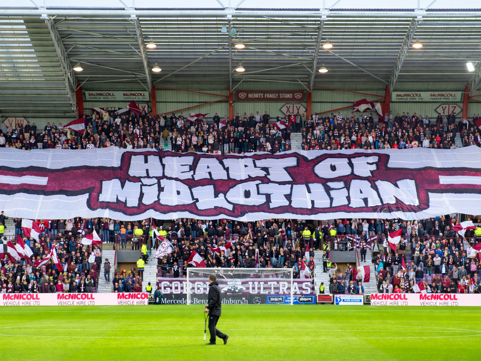 Een grote menigte voetbalfans in een stadion houdt een enorm spandoek omhoog met de tekst "HEART OF MIDLOTHIAN."