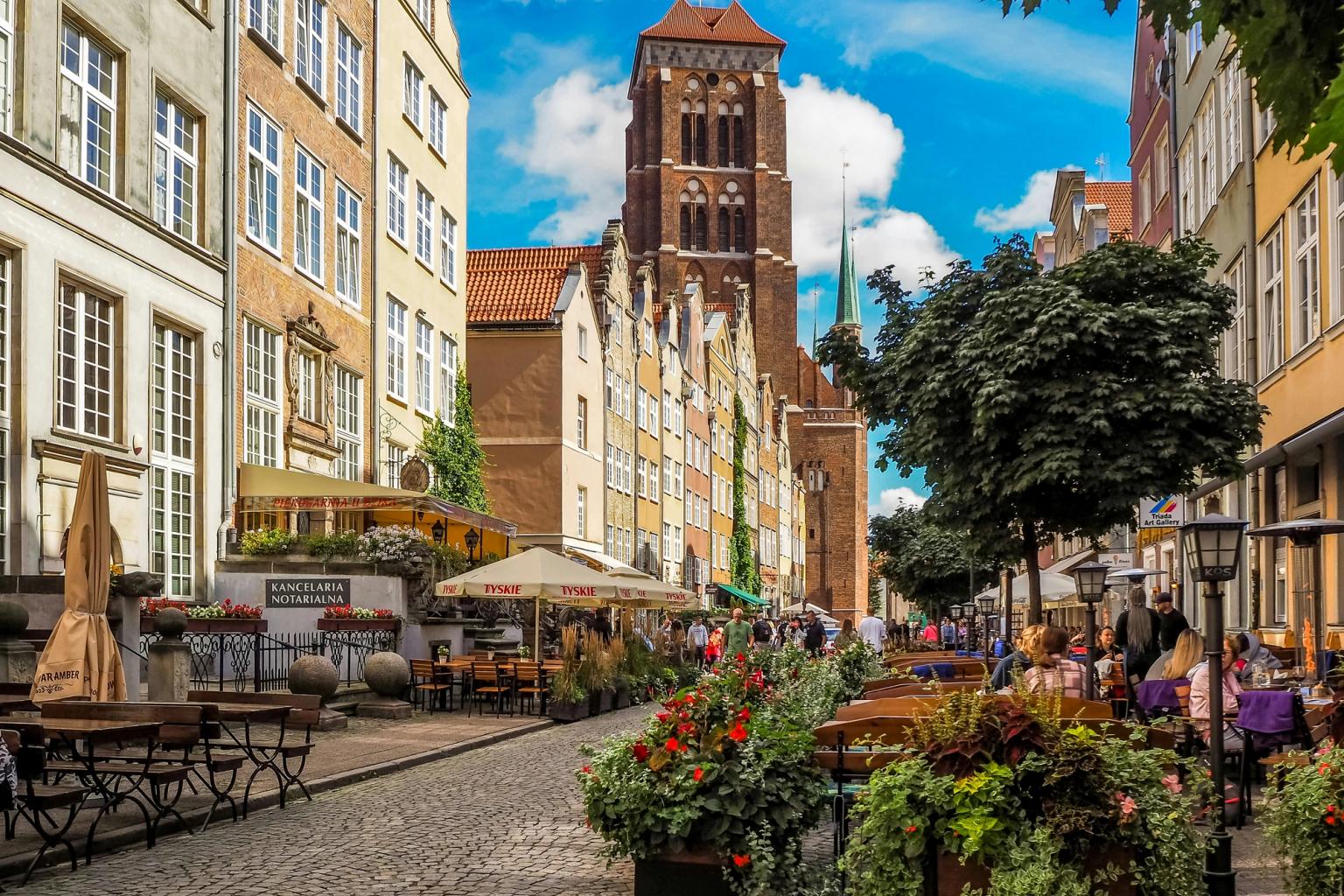 en smal brostensgade i en by med et tårn i baggrunden