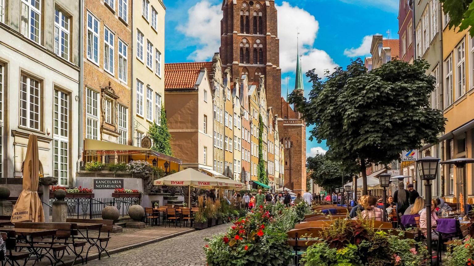 en smal brostensgade i en by med et tårn i baggrunden