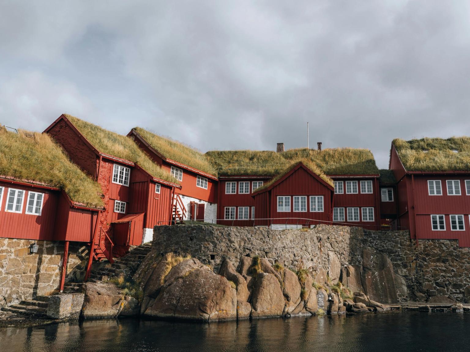 a group of red houses with grass on the roofs are next to a body of water