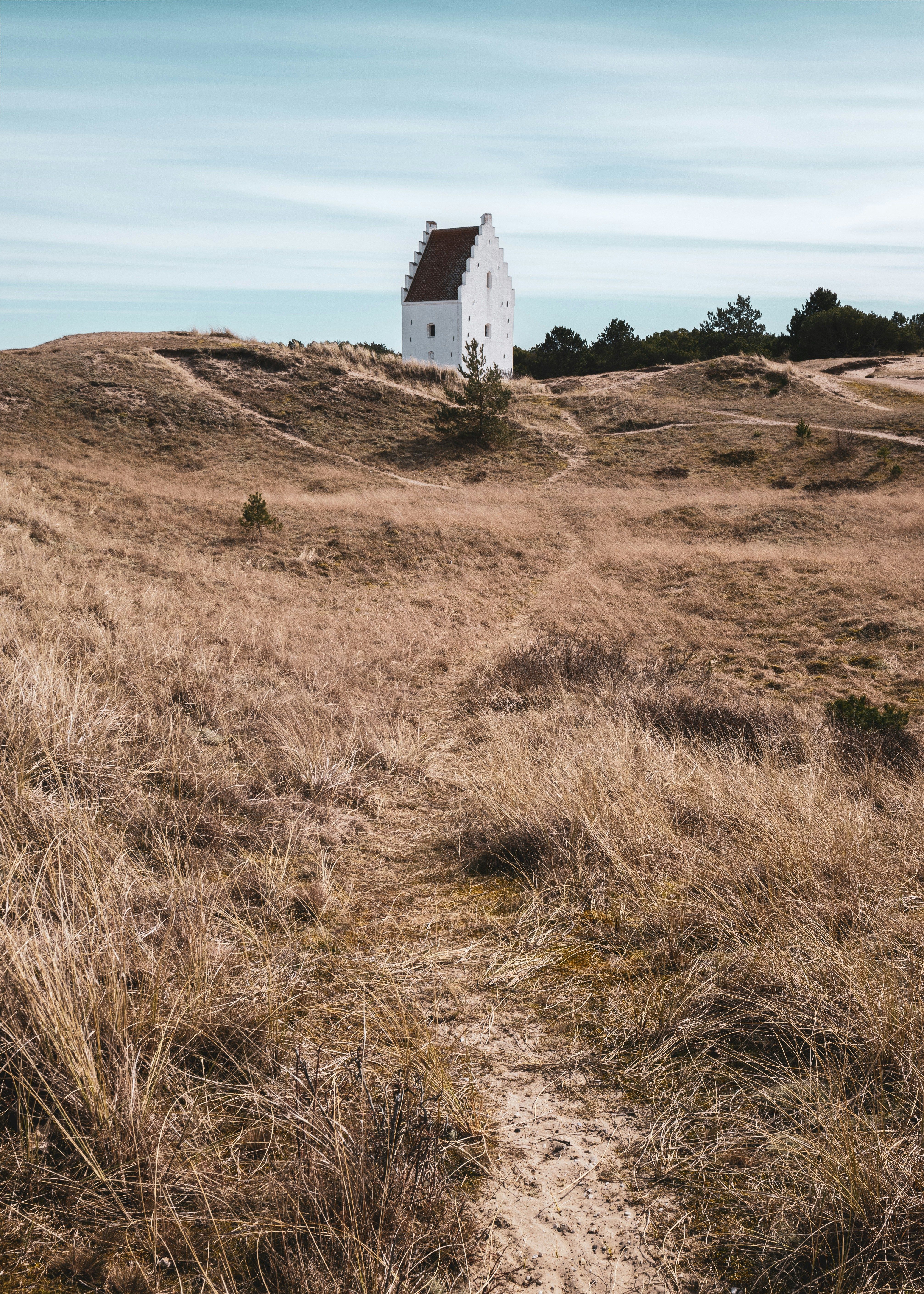 a small white house sits on top of a hill in the middle of a field