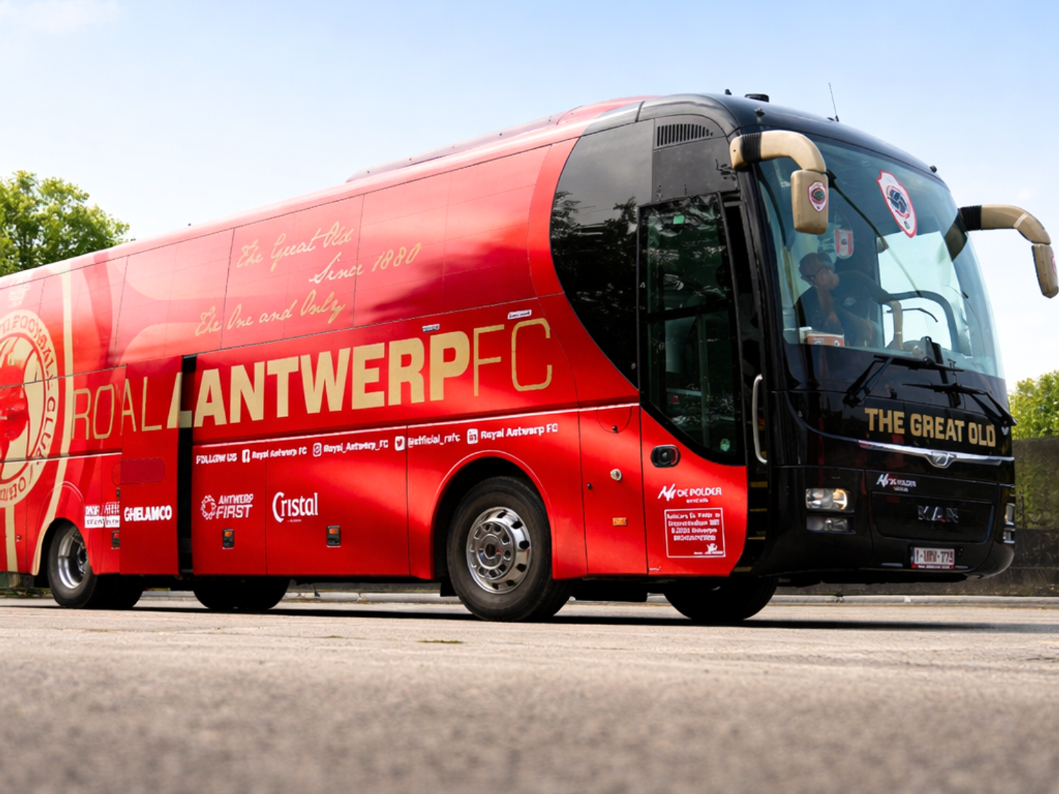 Ein rot-schwarzer Mannschaftsbus des Royal Antwerp FC steht auf Asphalt unter einem blauen Himmel.