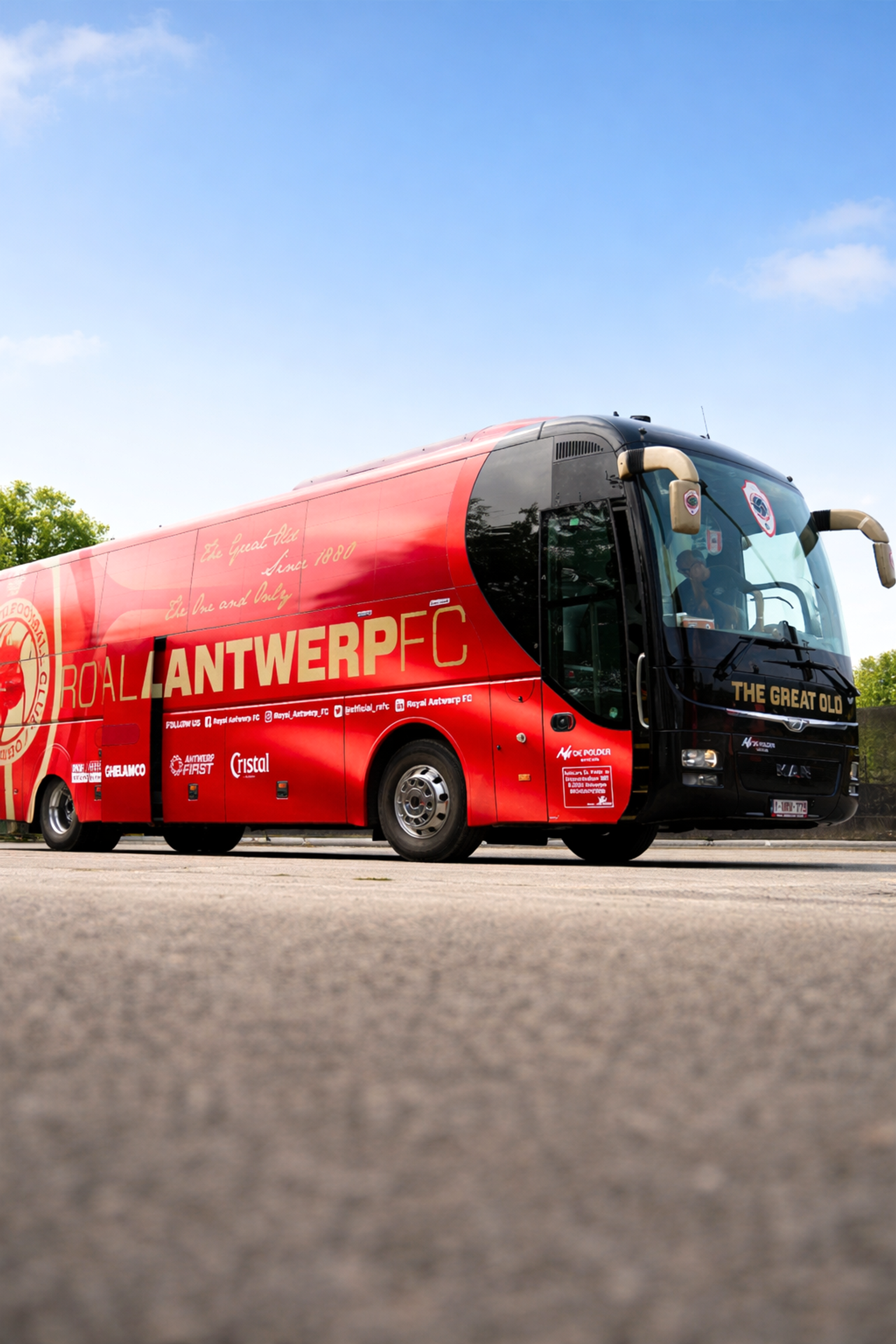 Ein rot-schwarzer Mannschaftsbus des Royal Antwerp FC steht auf Asphalt unter einem blauen Himmel.