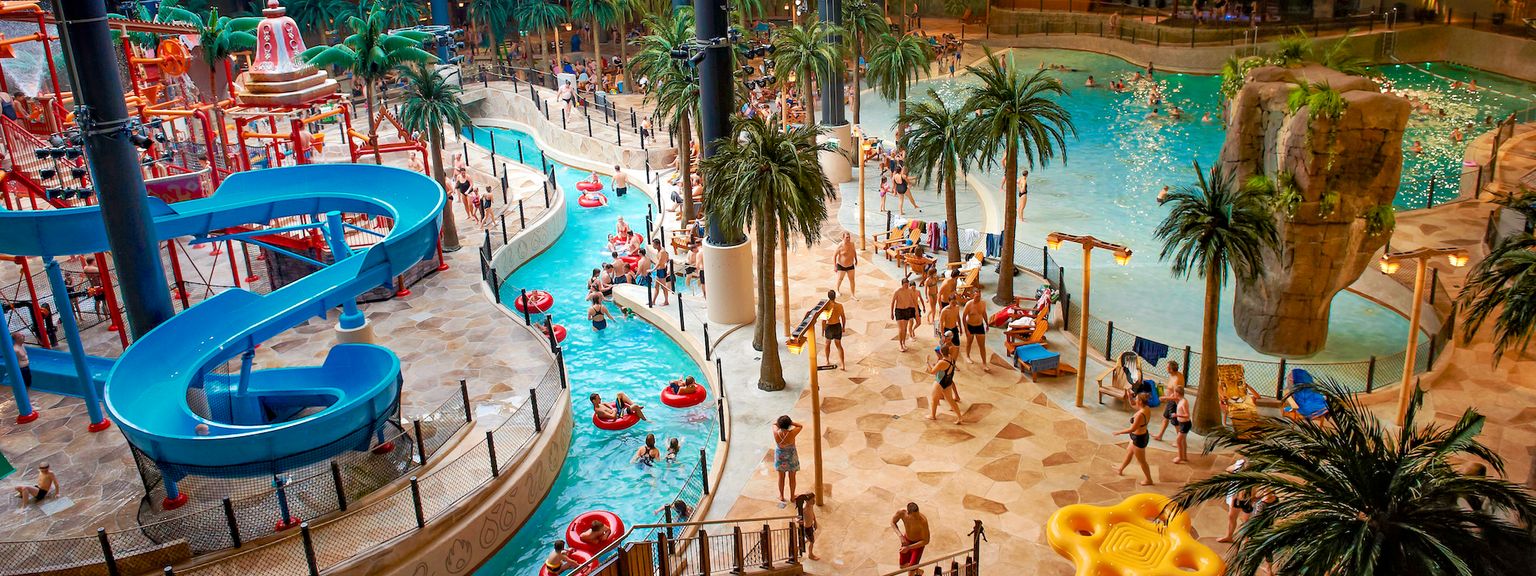 Zdjęcie z wnętrza największego parku wodnego w Skandynawii, Aquadome w Lalandia. Zdjęcie pokazuje obszar z basenami, zjeżdżalniami wodnymi i wieloma ludźmi.