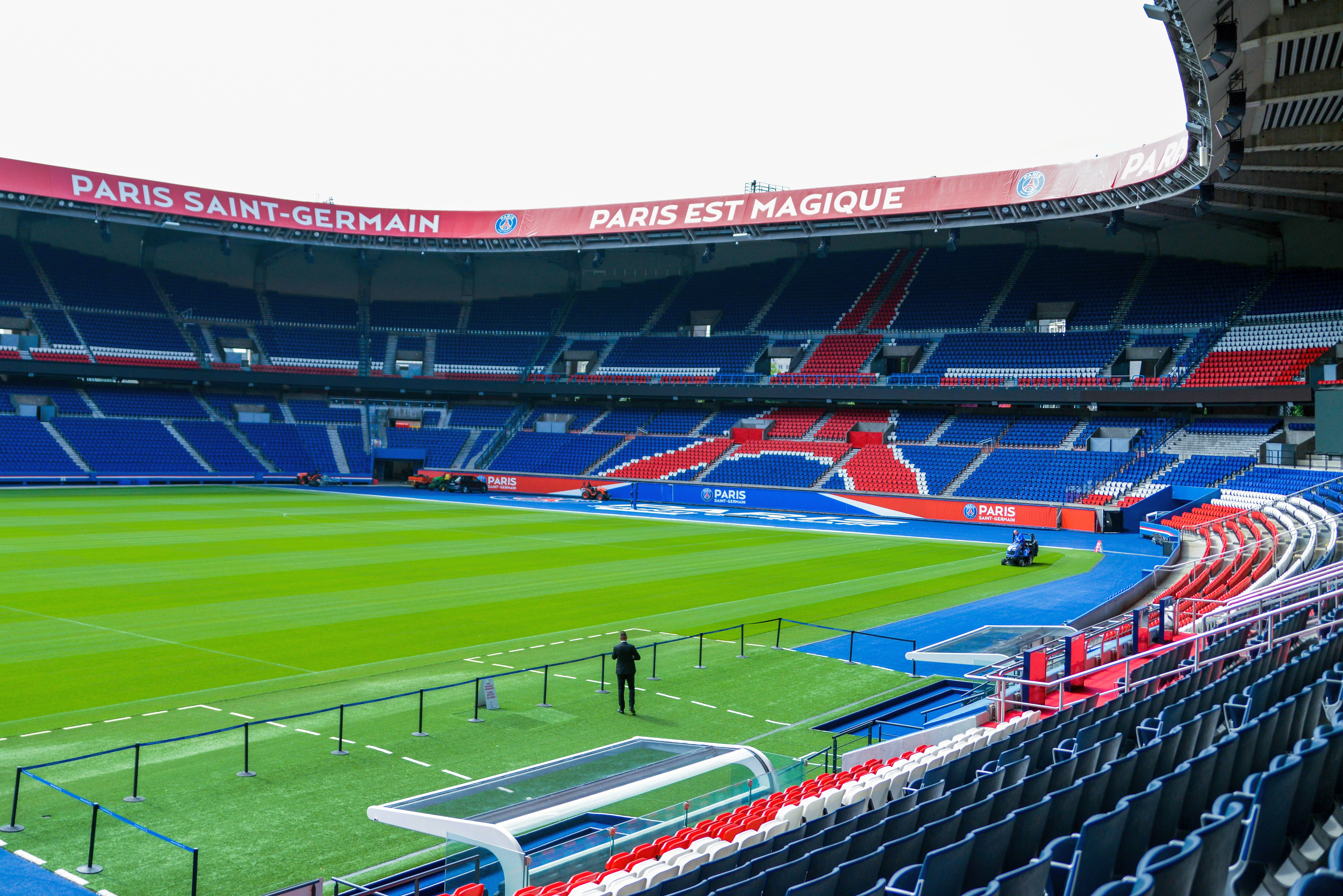 Empty Paris Saint-Germain football stadium with a green pitch and red and blue seating.
