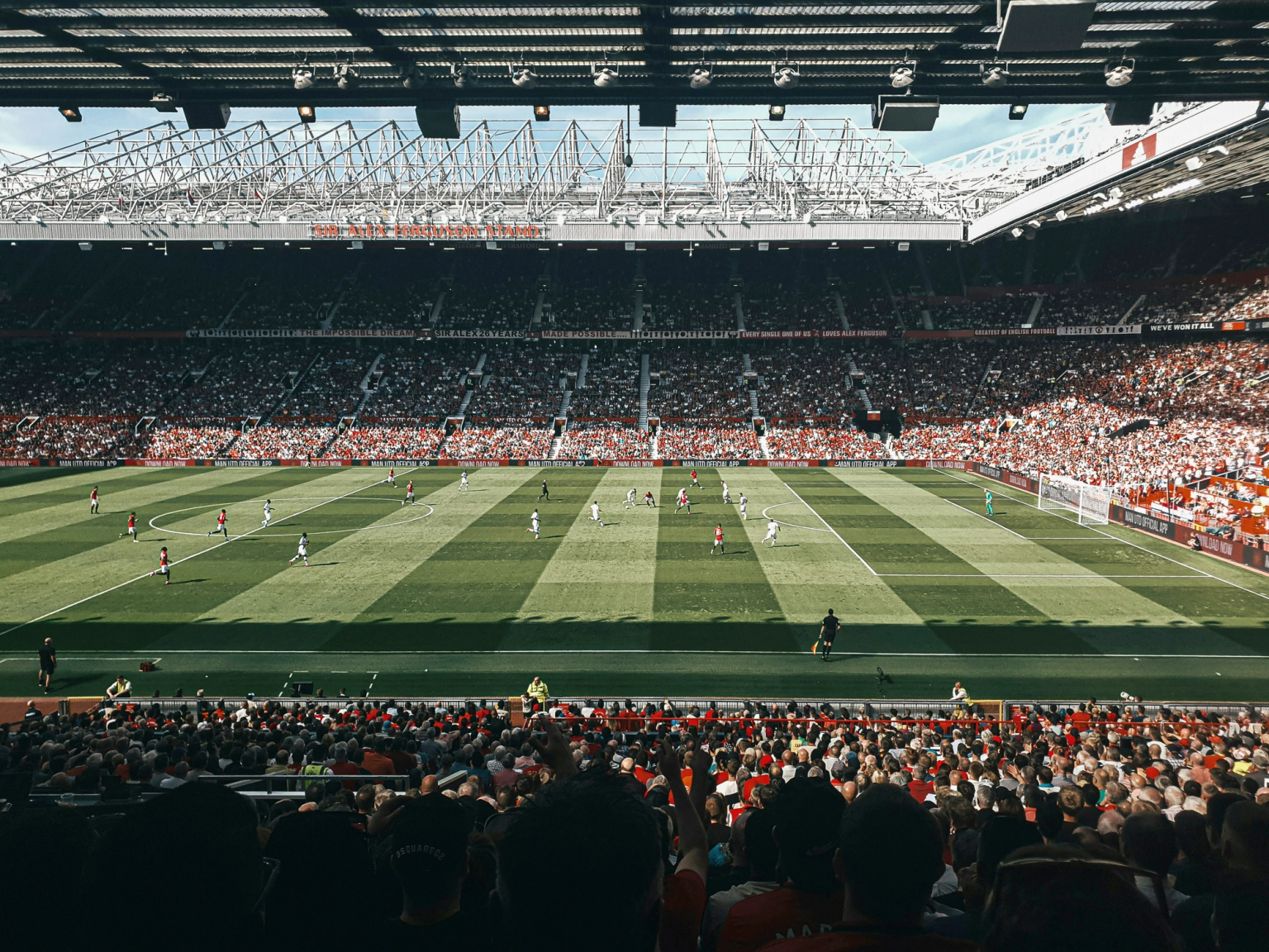 En fotballkamp på et fullsatt stadion med spillere på en stripete grønn bane.