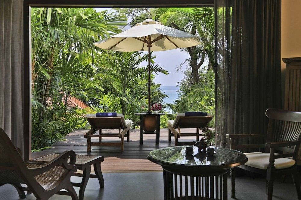 ein Raum mit Stühlen, einem Tisch, einem Regenschirm und Blick auf das Meer.