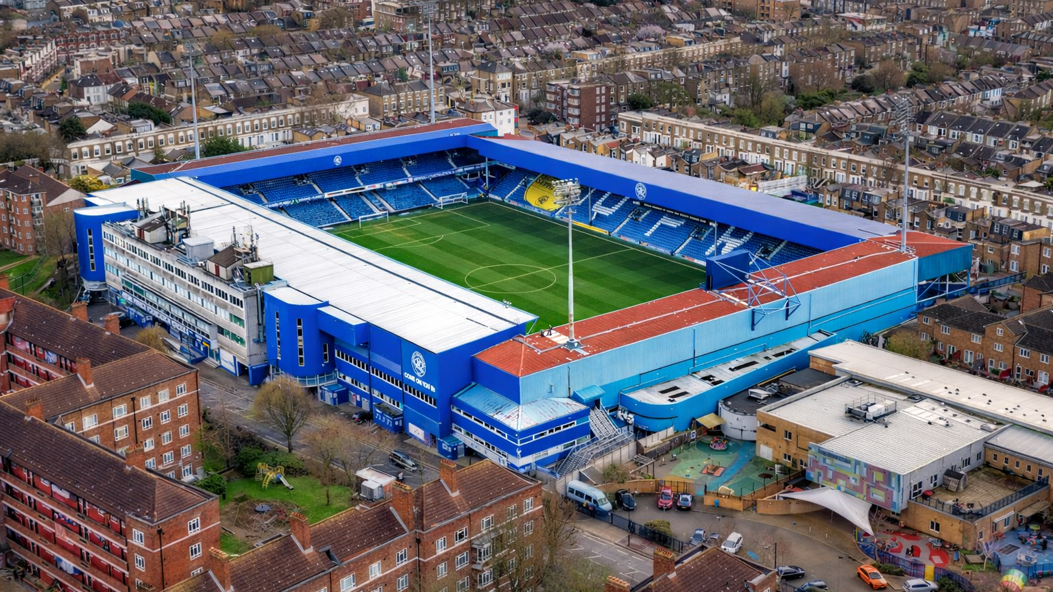 Vista aérea de un estadio de fútbol azul y blanco rodeado de edificios residenciales.