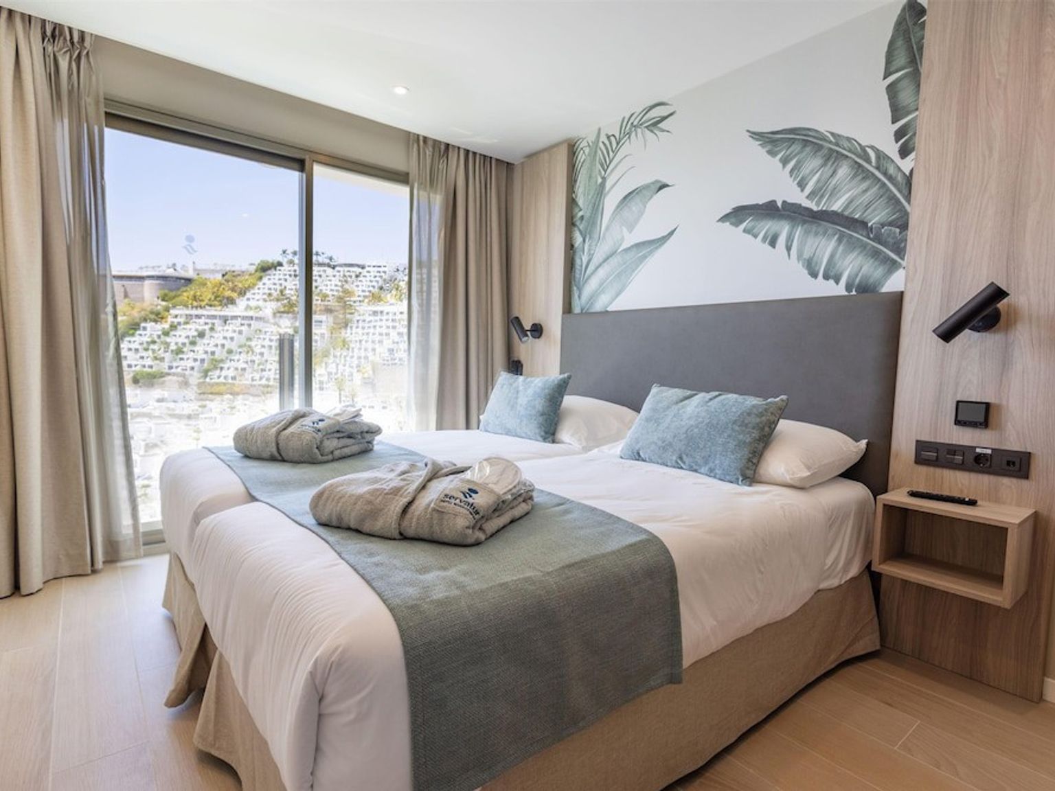 Et moderne dobbeltværelse med en tropisk vægmaleri og en naturskøn udsigt over bakkerne fra vinduet.