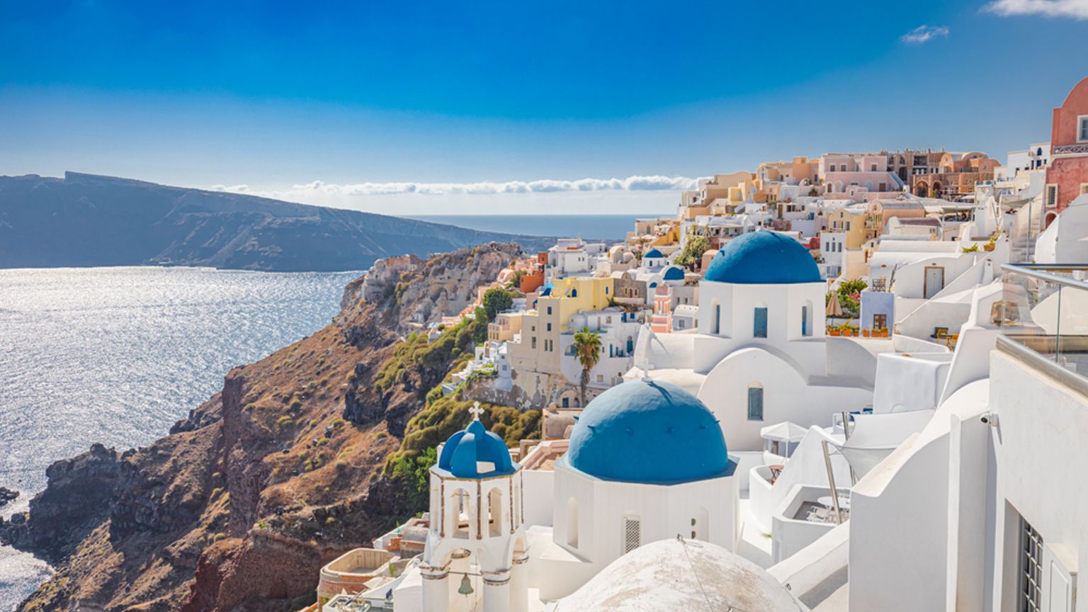 Hvide klippebygninger med blå kupler i Santorini med udsigt over Det Ægæiske Hav.