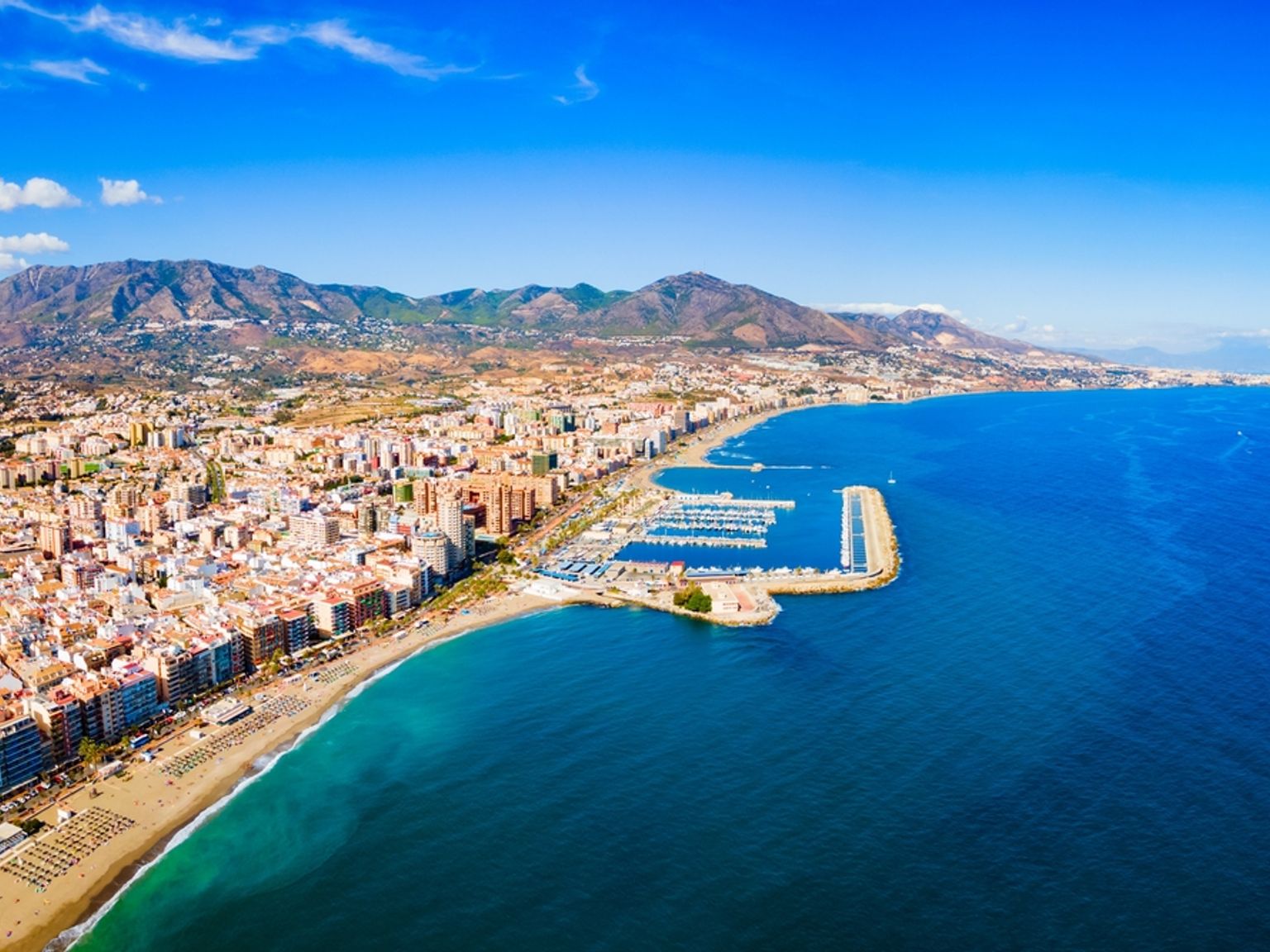 et luftfoto av en by ved siden av havet med fjell i bakgrunnen