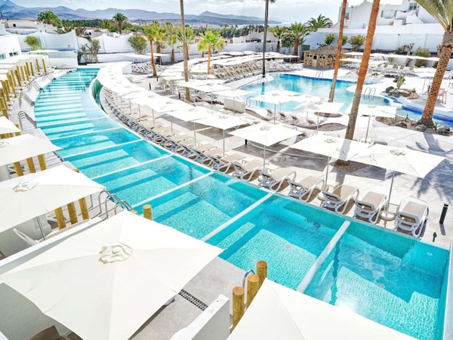 en stor simbassäng omgiven av paraplyer och stolar på ett hotell