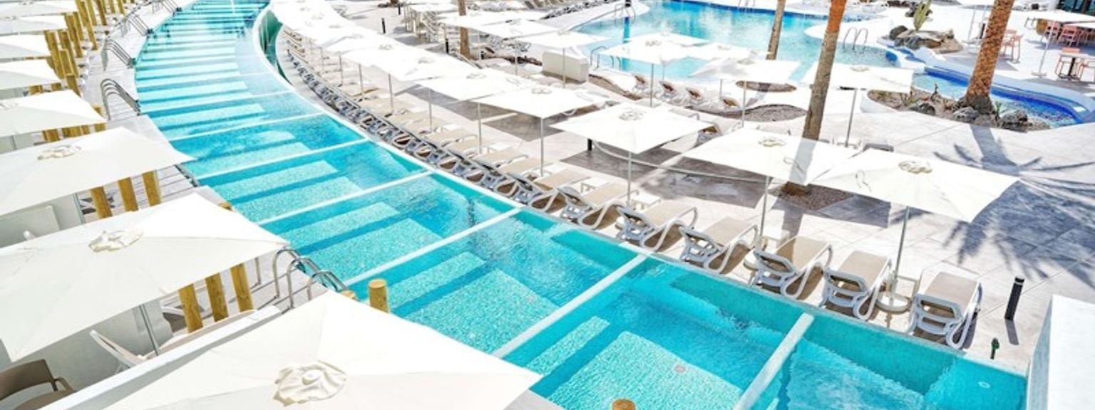 en stor simbassäng omgiven av paraplyer och stolar på ett hotell