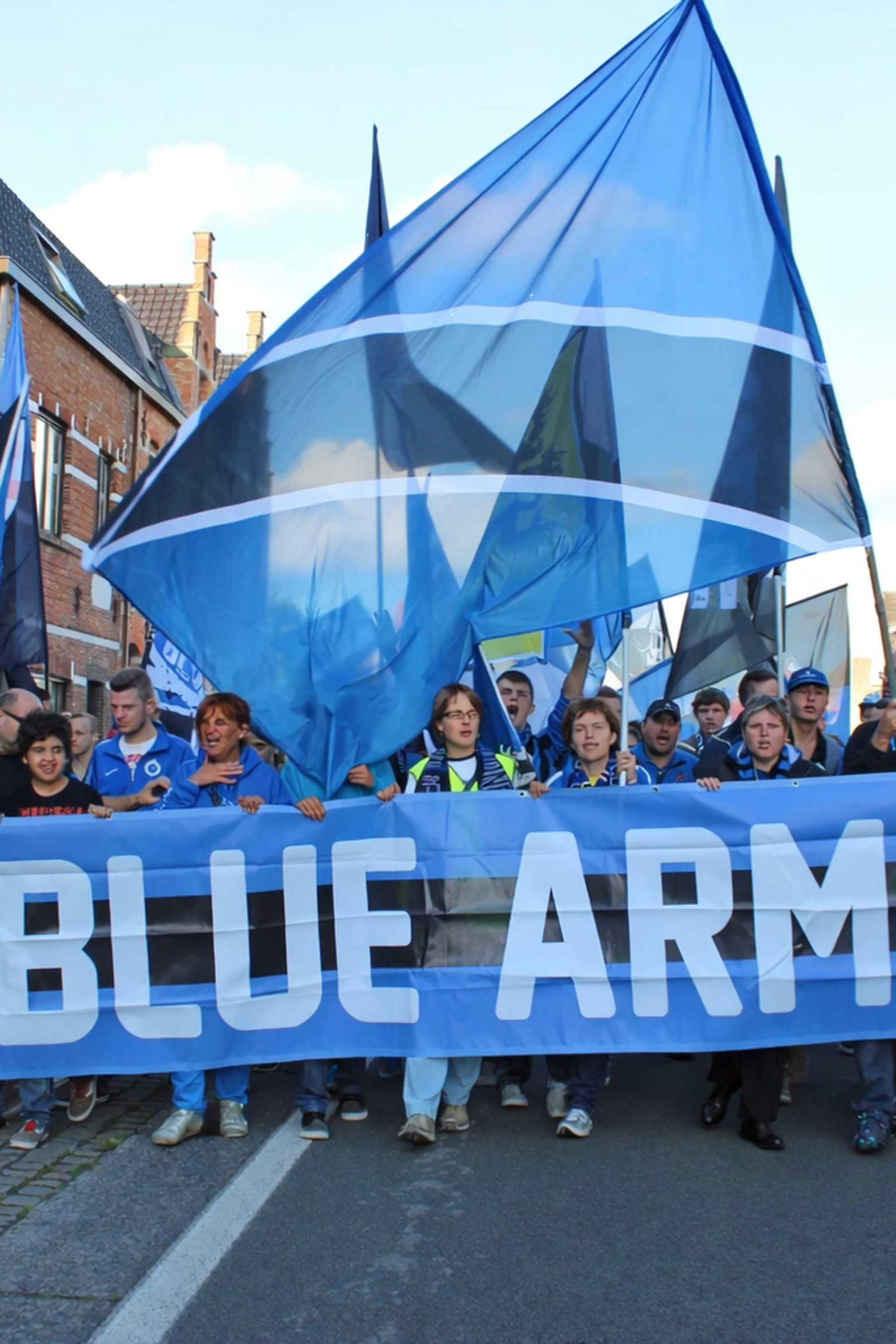 Ryhmä ihmisiä marssii kadulla kantaen lukuisia sinisiä lippuja ja banderollia, jossa lukee "BLUE ARMY" ja jossa on leijonaembleemi.