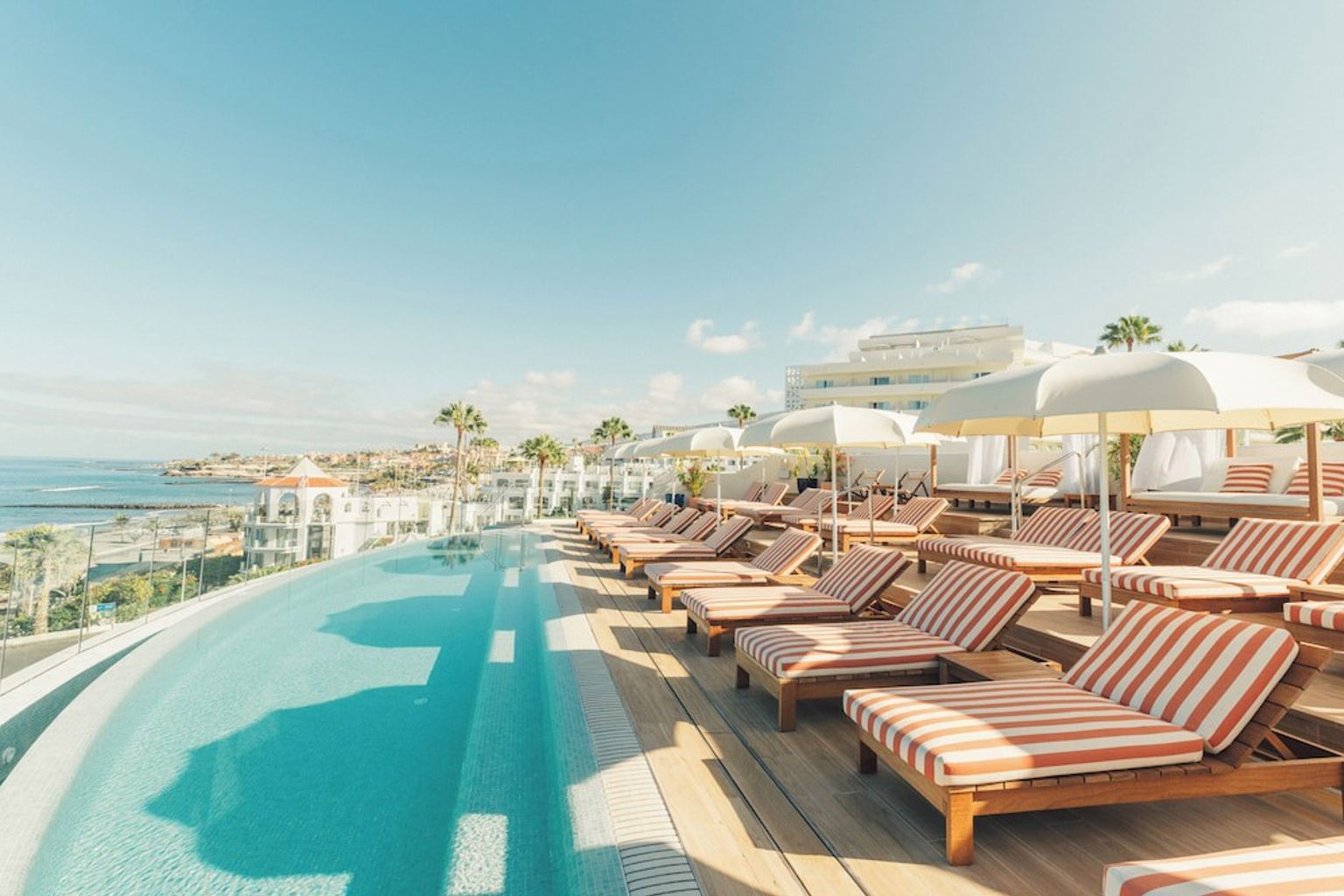 en swimmingpool omgiven av randiga stolar och parasoller med utsikt över havet