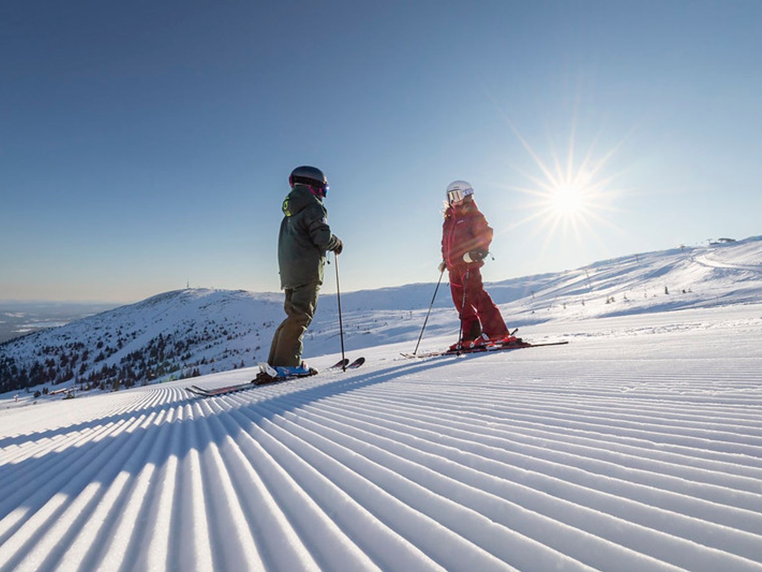 to personer står på ski ned en snødekket bakke.