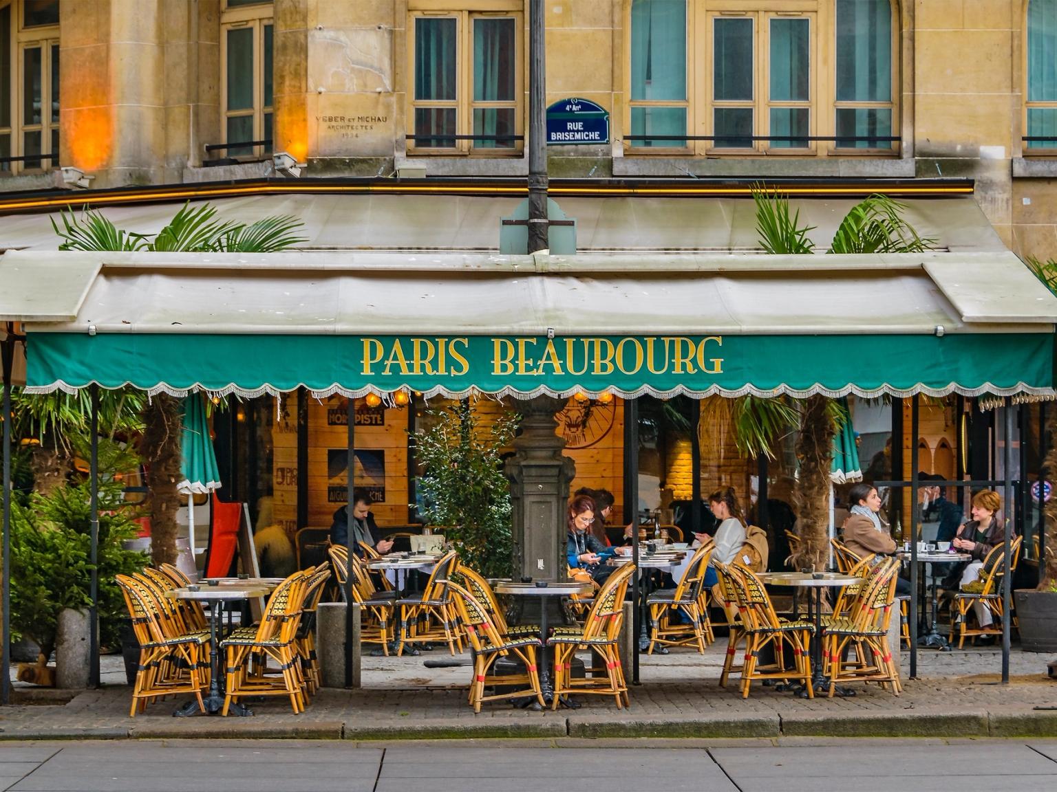 a group of people are sitting at tables outside of a restaurant in Paris