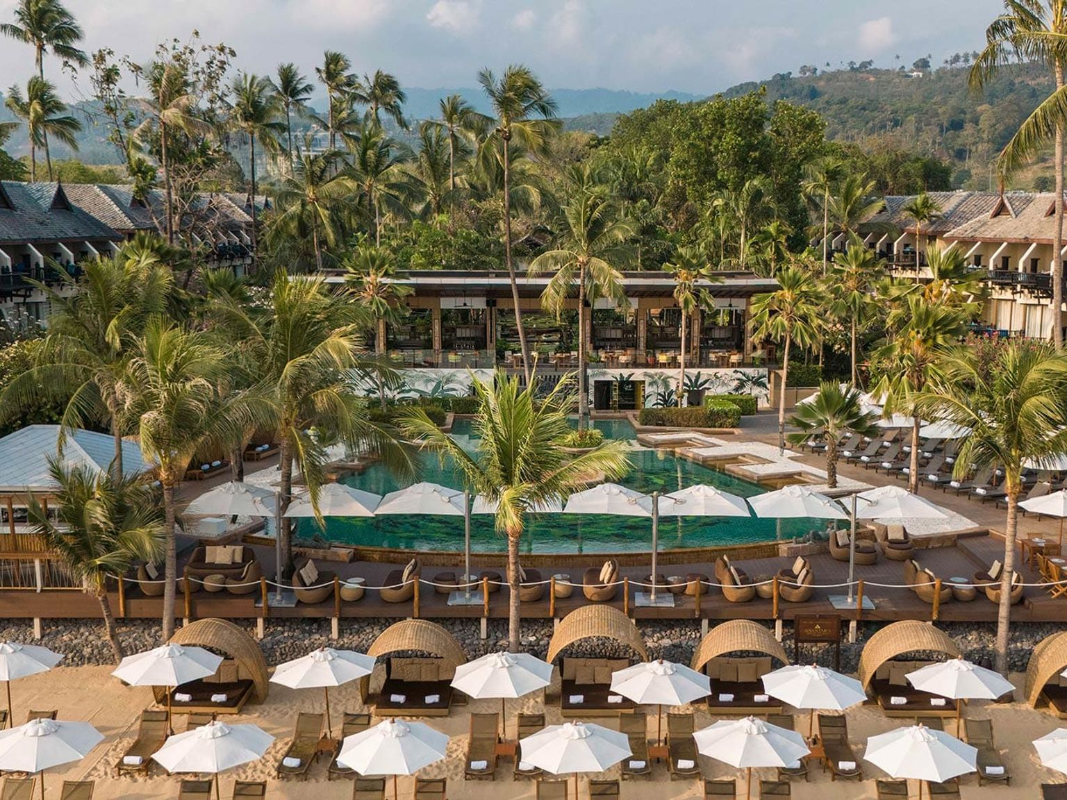en flygvy av en tropisk resort med en stor pool och parasoller på stranden