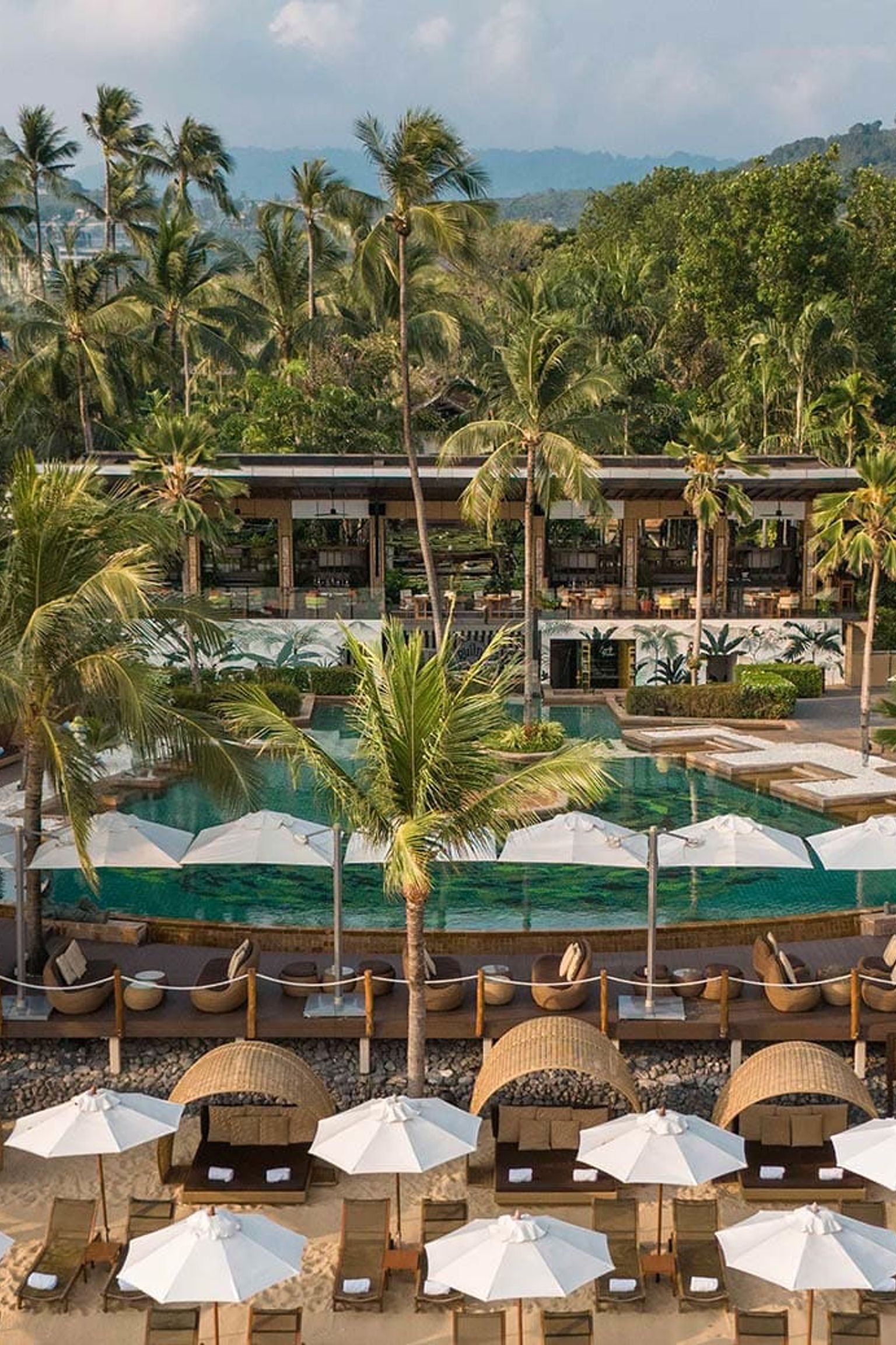 eine Luftaufnahme eines tropischen Resorts mit einem großen Pool und Sonnenschirmen am Strand