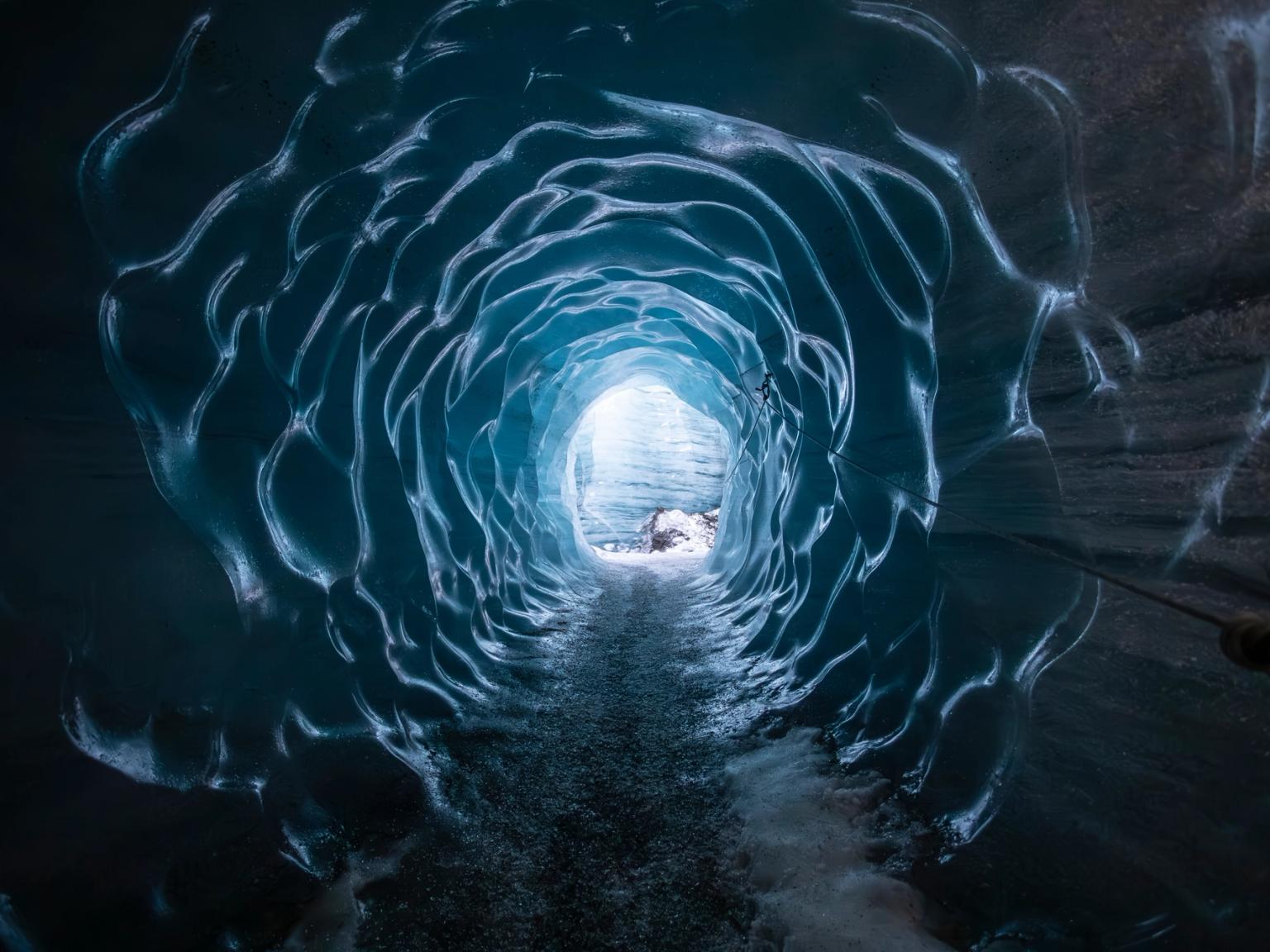 a person is walking through an ice cave with a light at the end