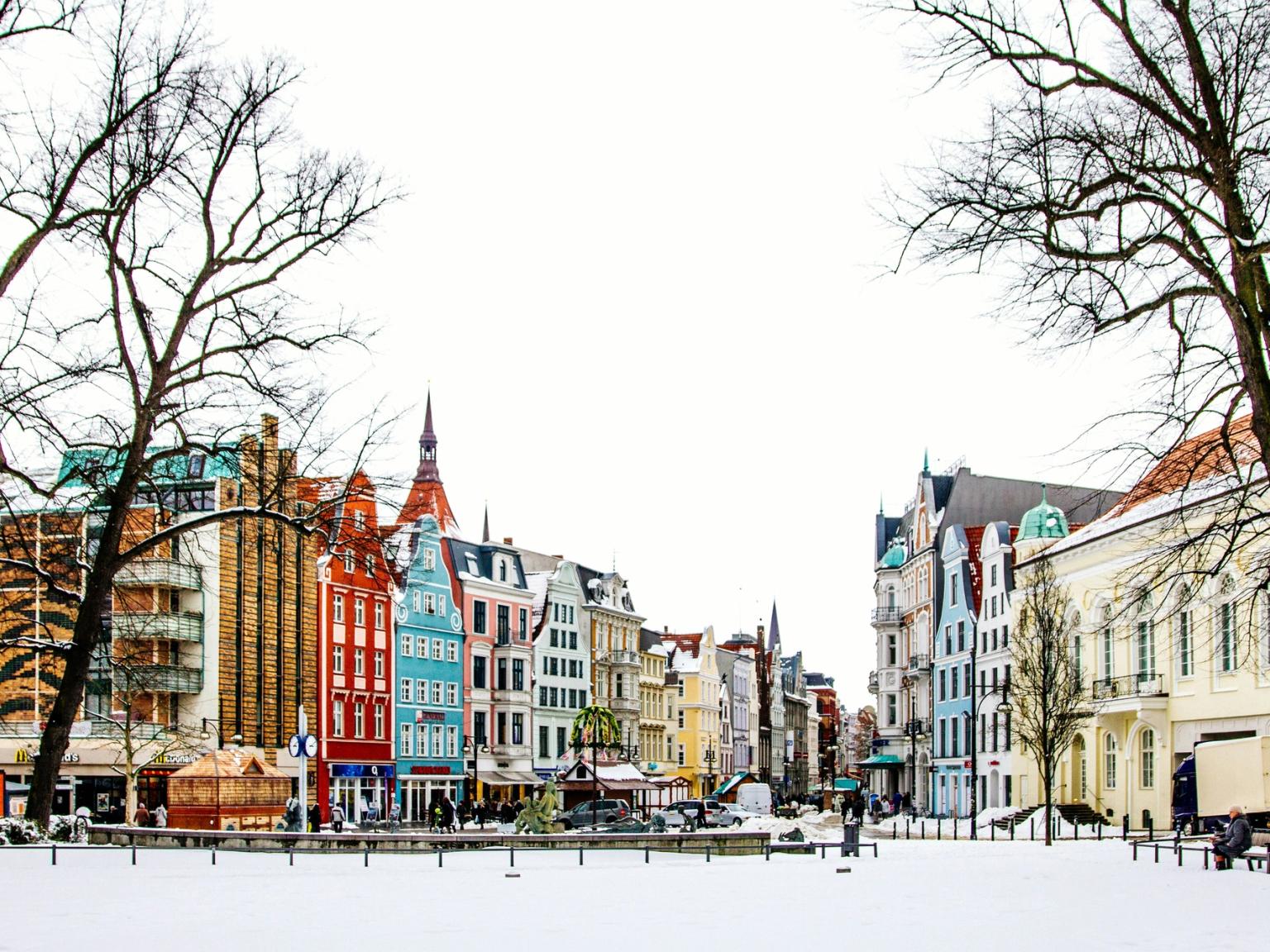 A snowy town square flanked by colorful historic buildings and bare trees.
