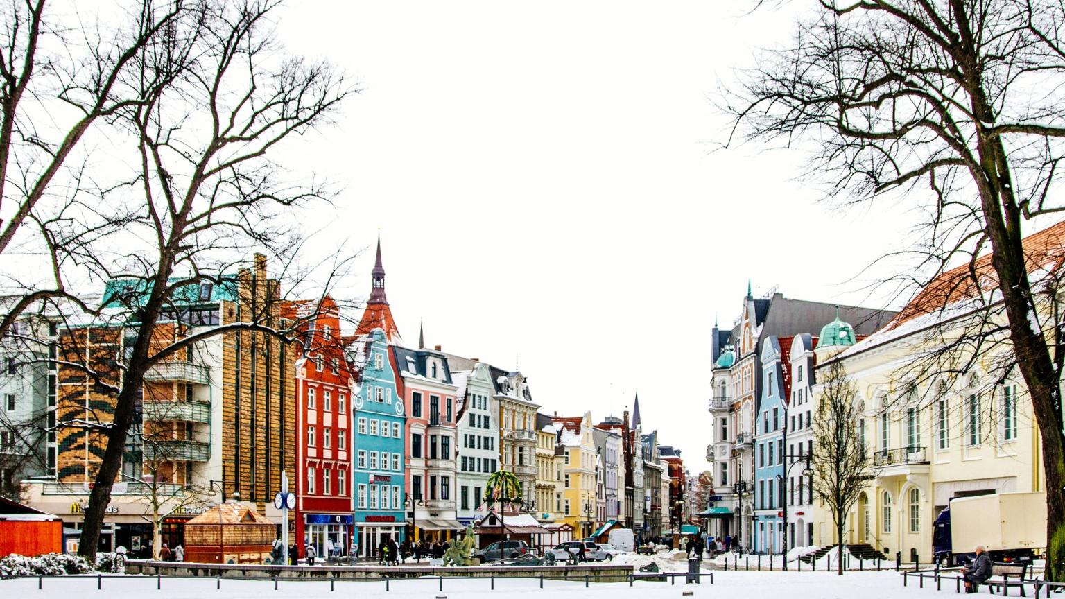 En sneklædt bytorv flankeret af farverige historiske bygninger og nøgne træer.