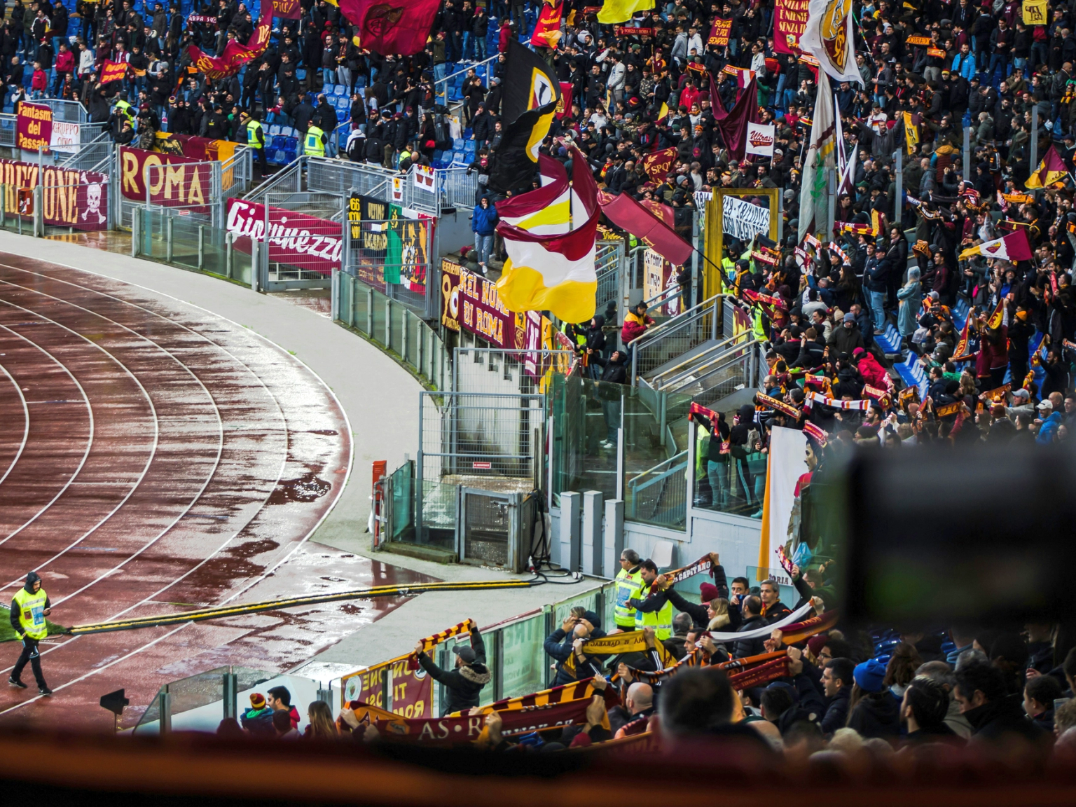 Energiske fans som vifter med flagg og bannere på et stadion med en våt løpebane.