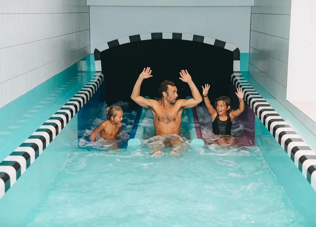 En man och två barn som glatt åker nerför en vattenrutschbana.