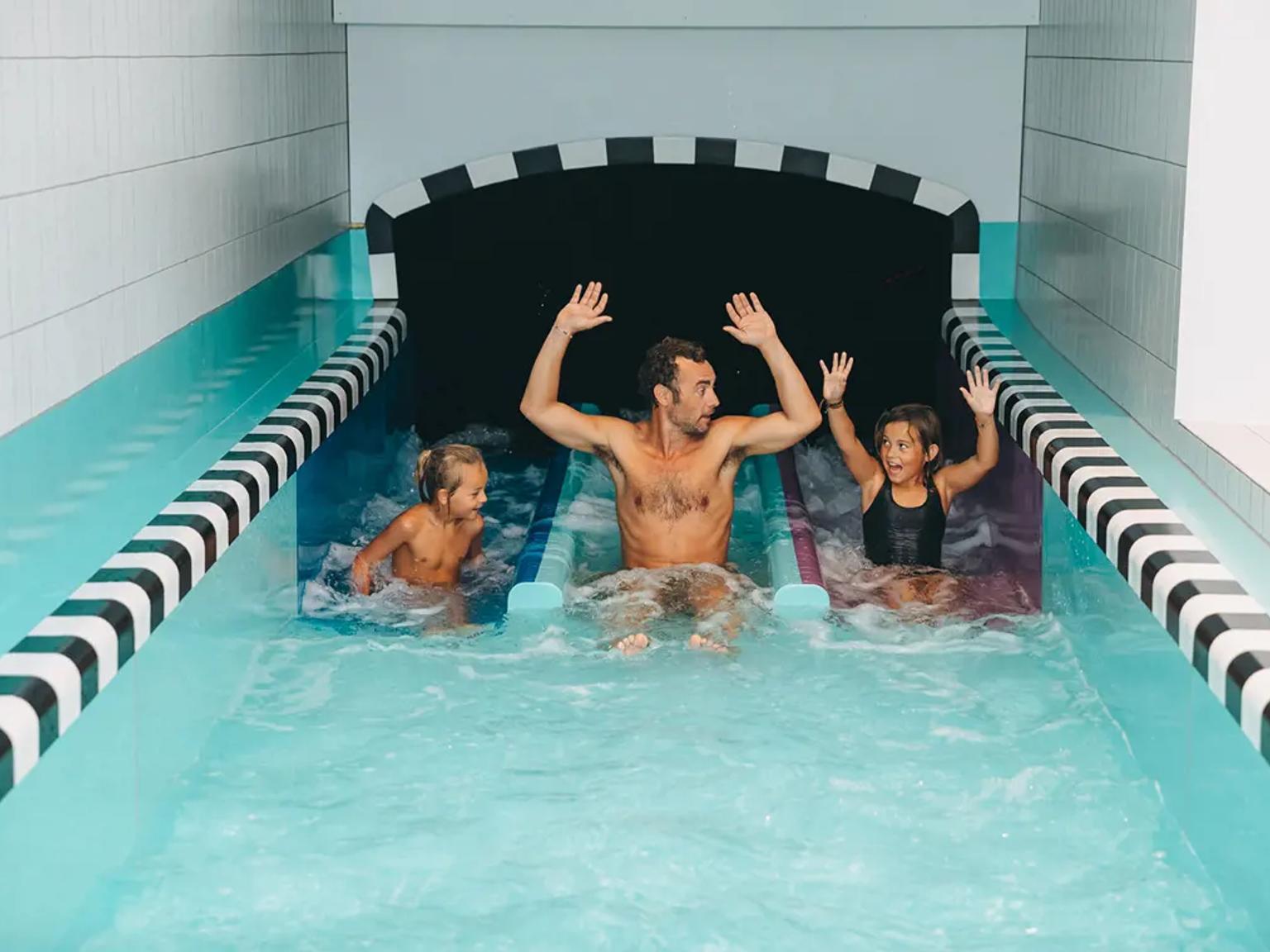 En mann og to barn som gledelig kommer ned en vannsklie.