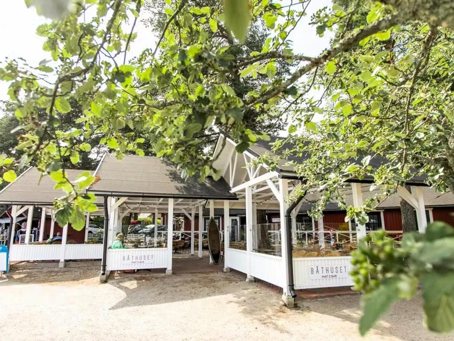 A red and white building with an outdoor patio nestled among green trees on a sunny day.