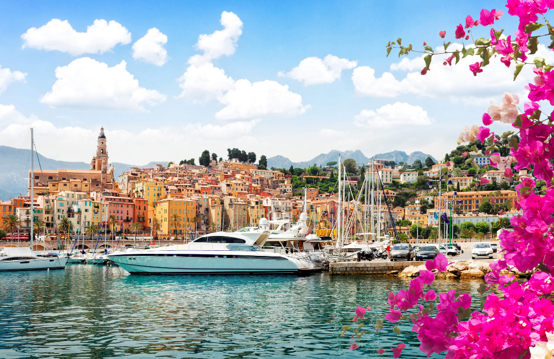 Livlig medelhavshamn på Franska rivieran med färgglada byggnader, lyxyachter och rosa blommor.