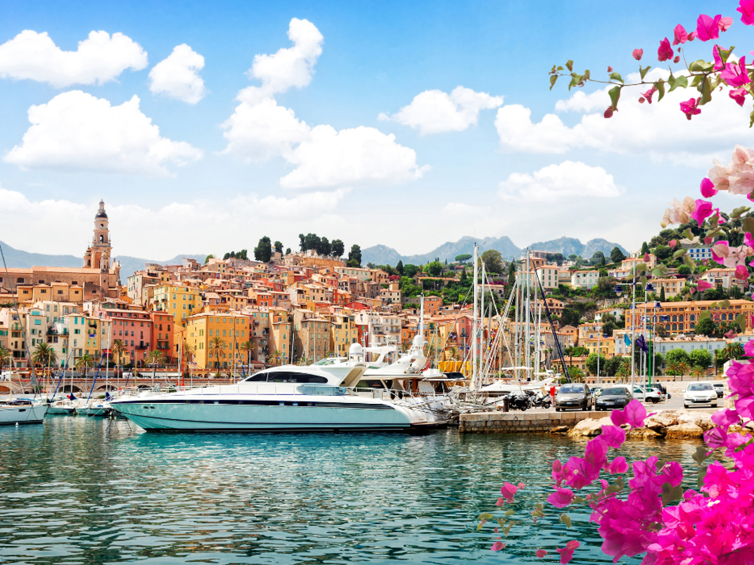 Livlig medelhavshamn på Franska rivieran med färgglada byggnader, lyxyachter och rosa blommor.