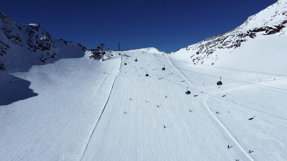 Solrik skibakke med skiløpere, gondoler og snødekte fjell.