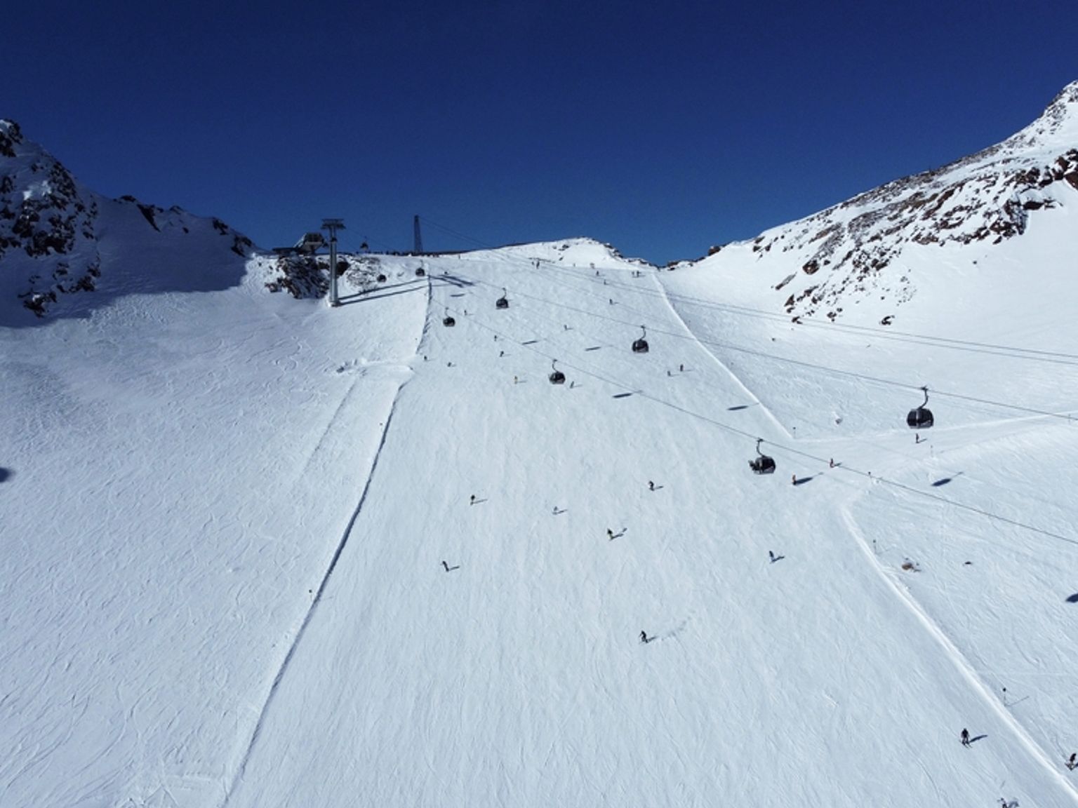Solrik skibakke med skiløpere, gondoler og snødekte fjell.