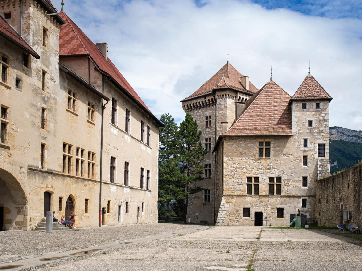 et stort steinslott med et rødt flislagt tak og en gårdsplass foran det