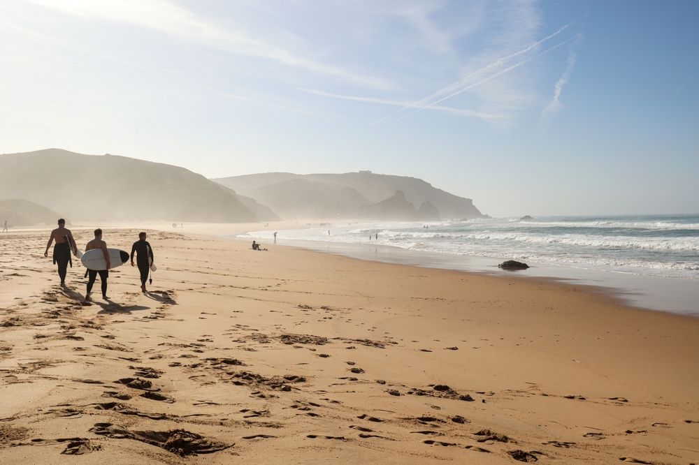 a group of people are walking on a beach carrying surfboards.