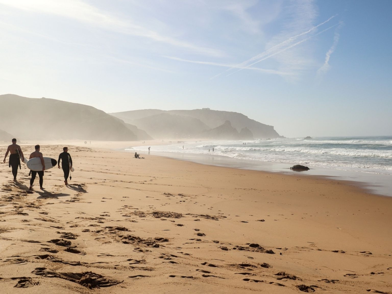 a group of people are walking on a beach carrying surfboards.