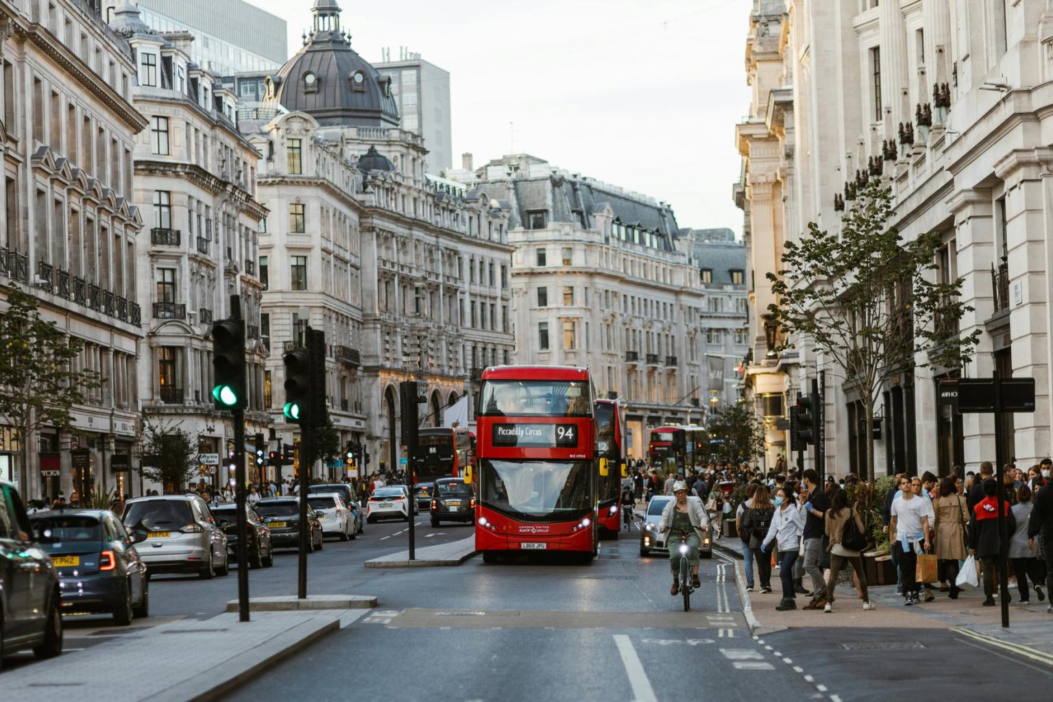 en röd dubbeldäckare kör nerför en livlig stadsgata i London.