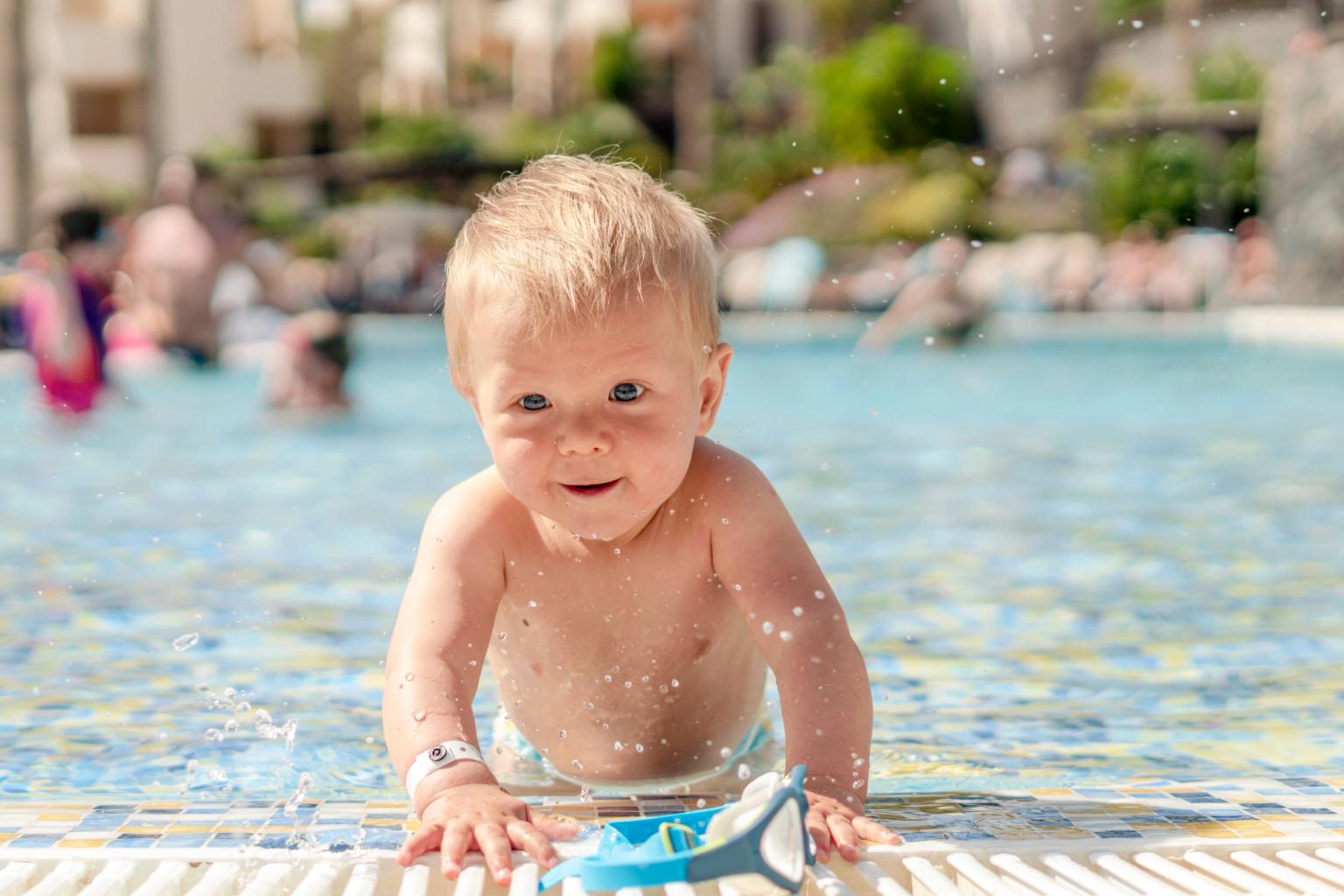 En smilende blond baby, der plasker i en swimmingpool.