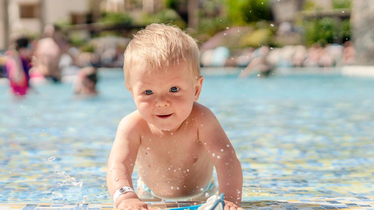 En smilende blond baby, der plasker i en swimmingpool.