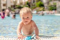 Ein lächelndes blondes Baby, das in einem Swimmingpool planscht.