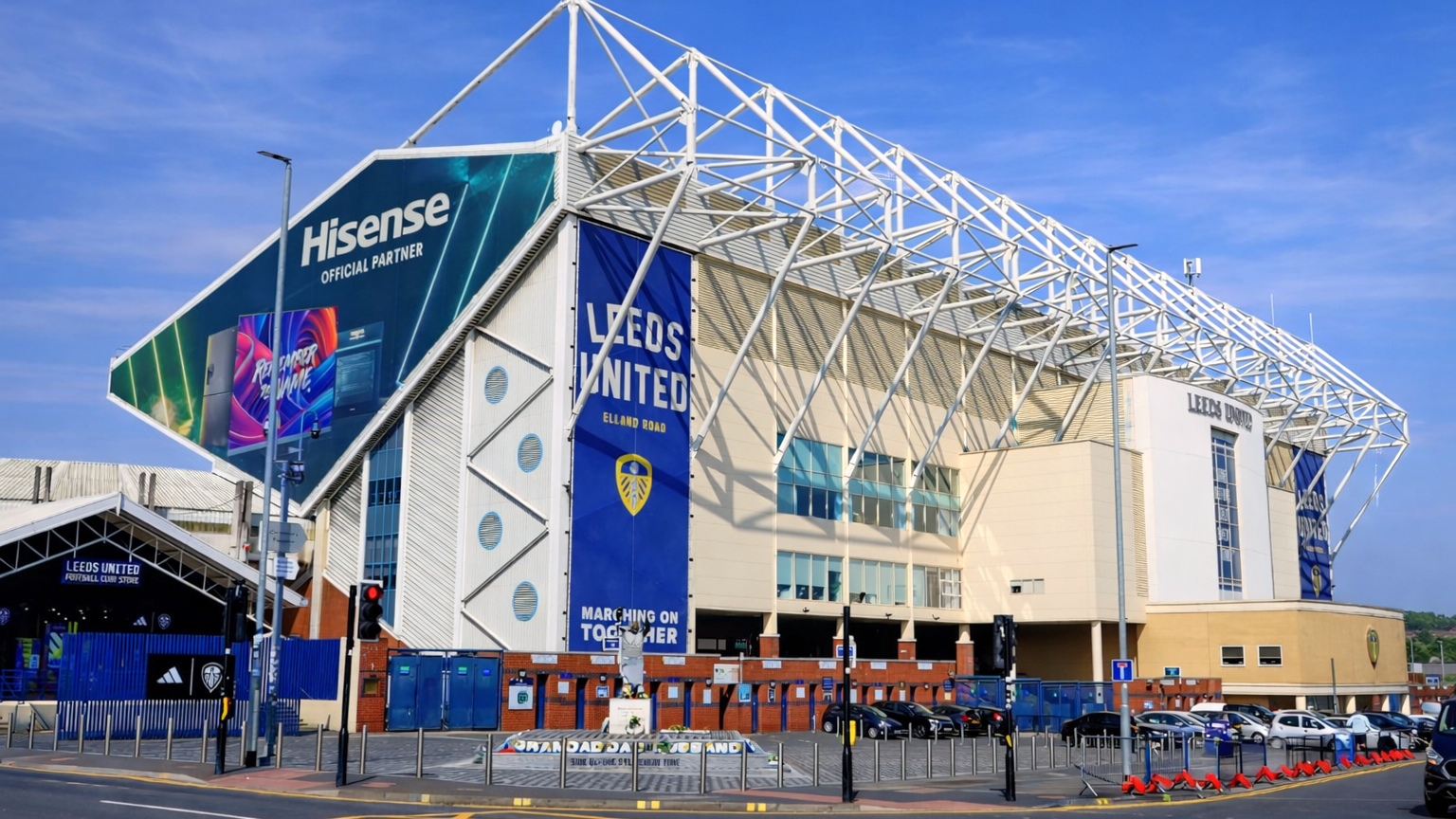 Elland Road stadium, home of Leeds United, with a large Hisense banner and white roof structure, viewed from the street.
