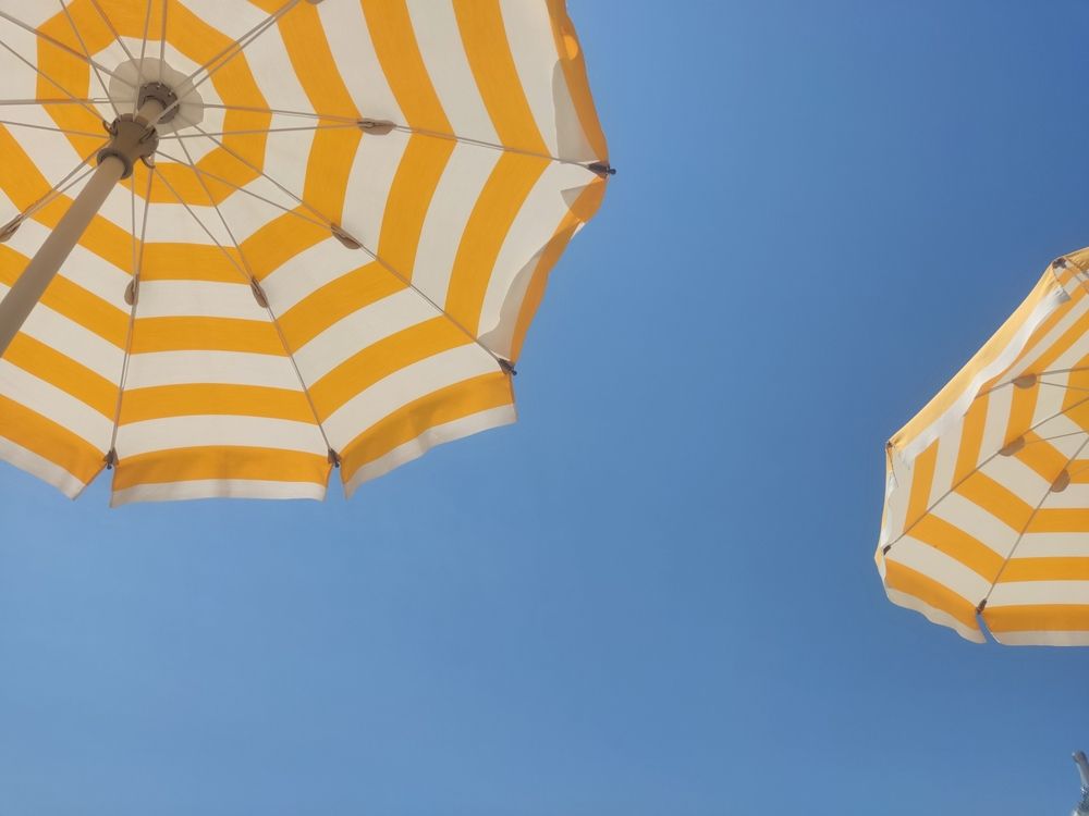 To gule og hvitstripete strandparasoller sett nedenfra mot en blå himmel.