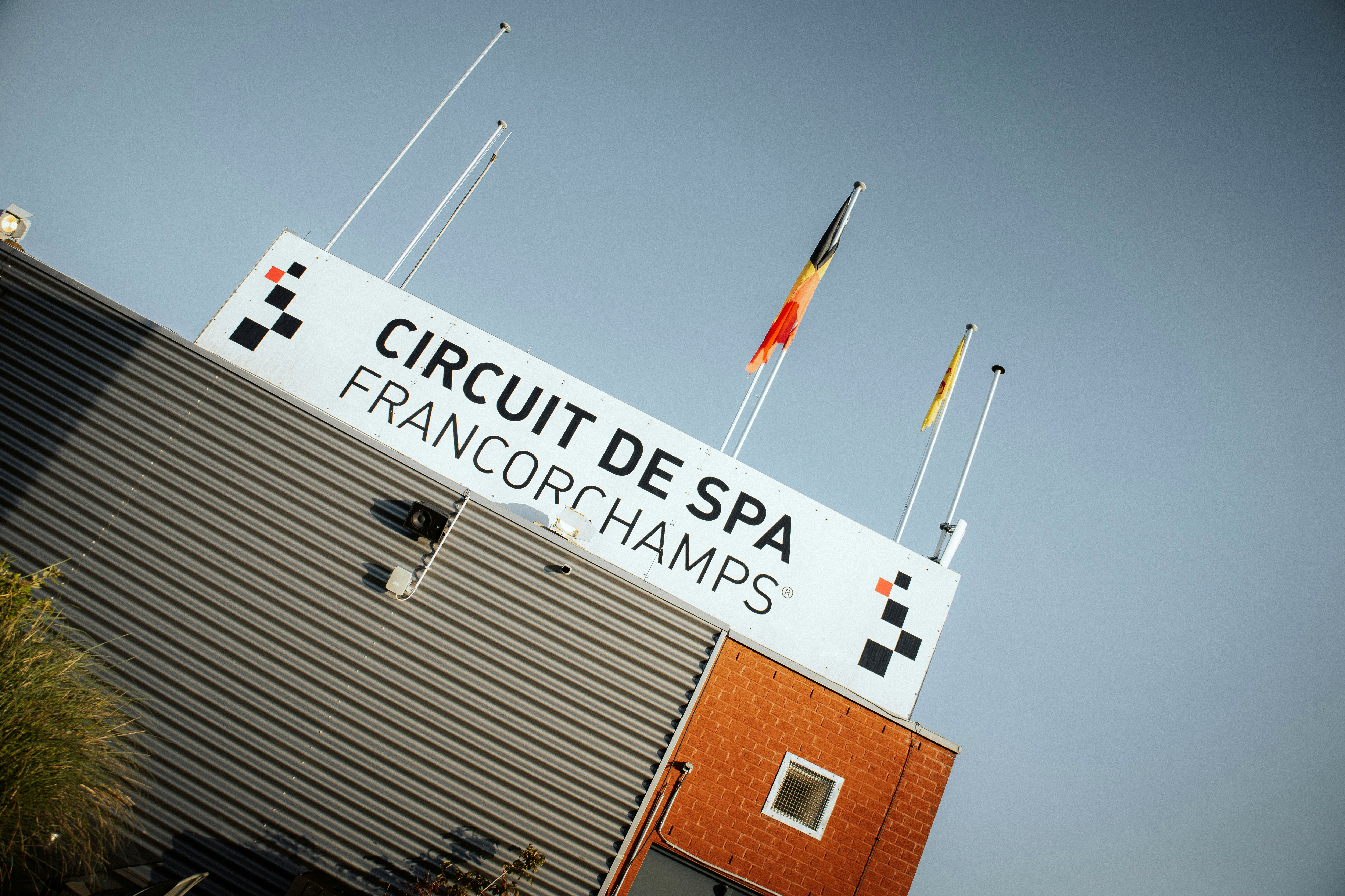 A sign for Circuit de Spa-Francorchamps on a building, with the Belgian flag and a yellow flag.