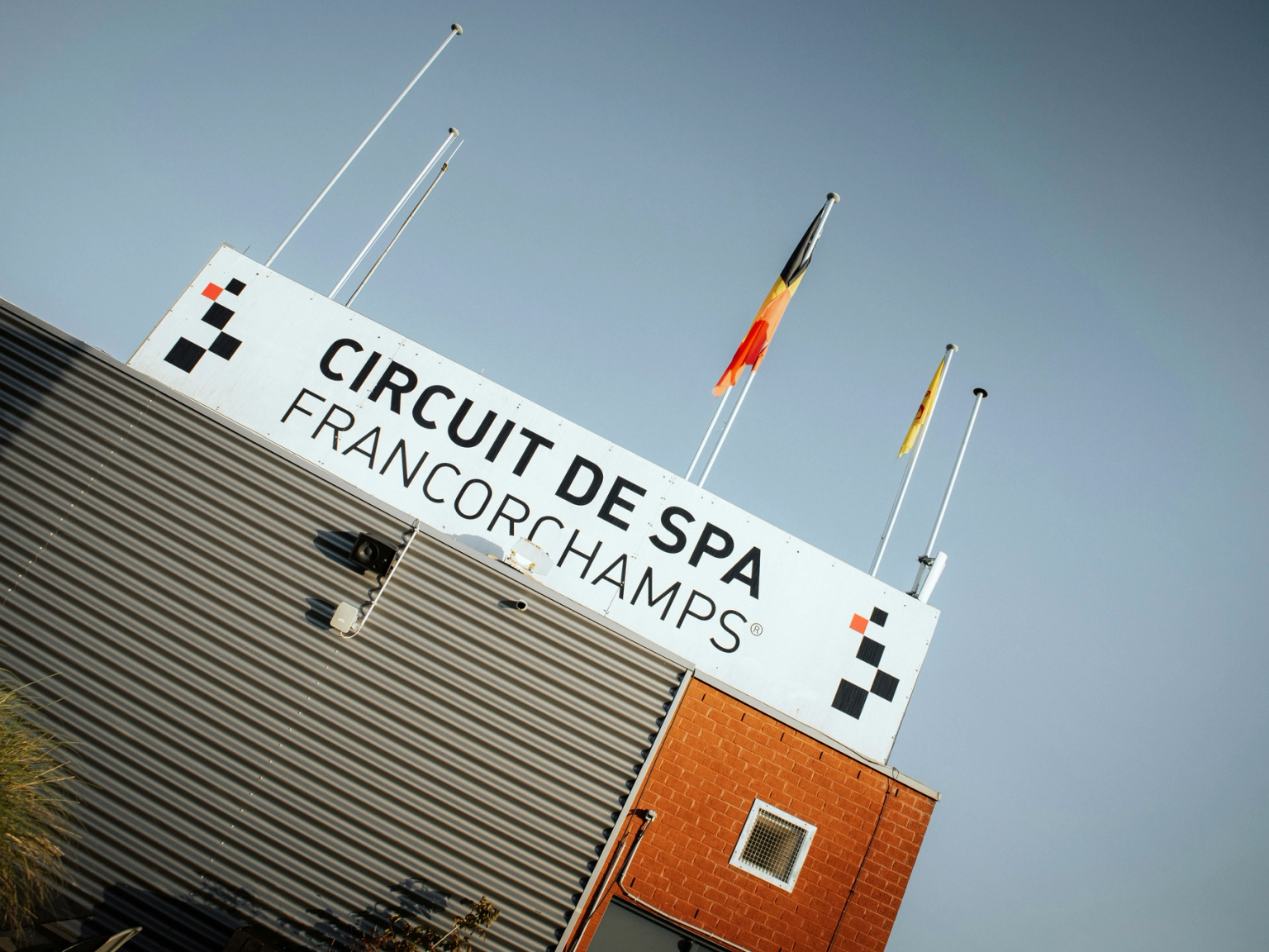 A sign for Circuit de Spa-Francorchamps on a building, with the Belgian flag and a yellow flag.