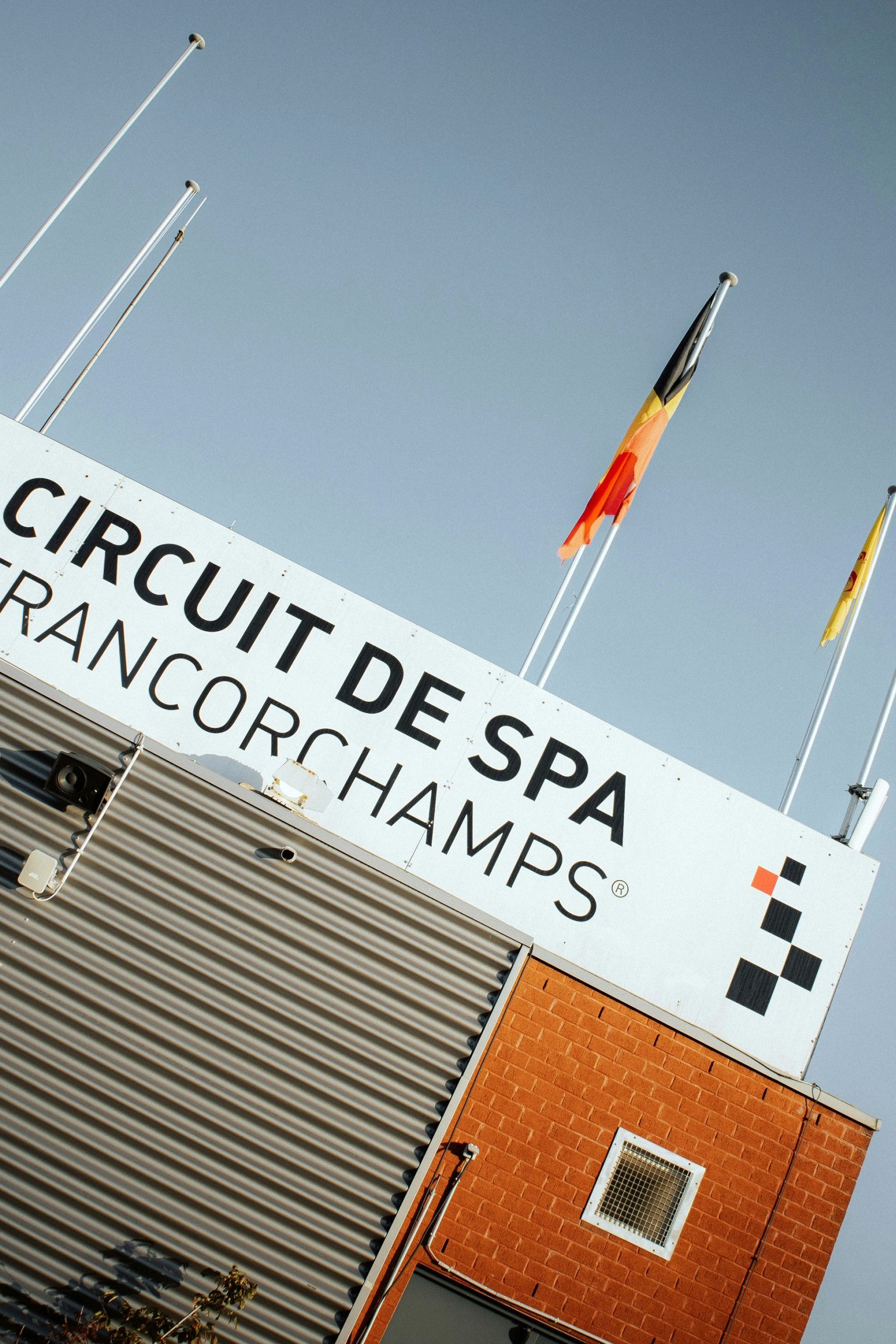 A sign for Circuit de Spa-Francorchamps on a building, with the Belgian flag and a yellow flag.